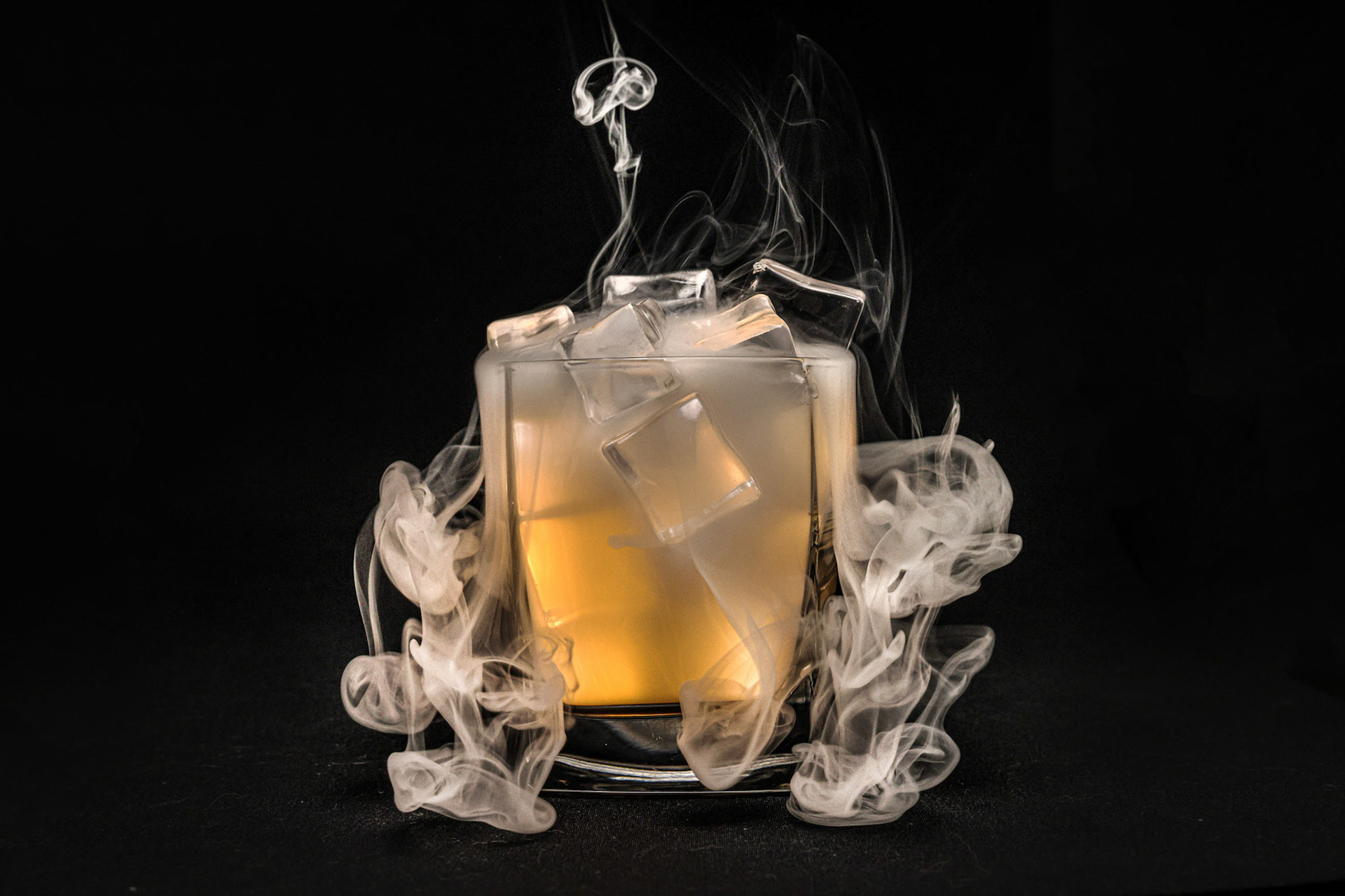 Opaque transparent ice filled drink short glass yellow tungsten light flame smoke fog on black background