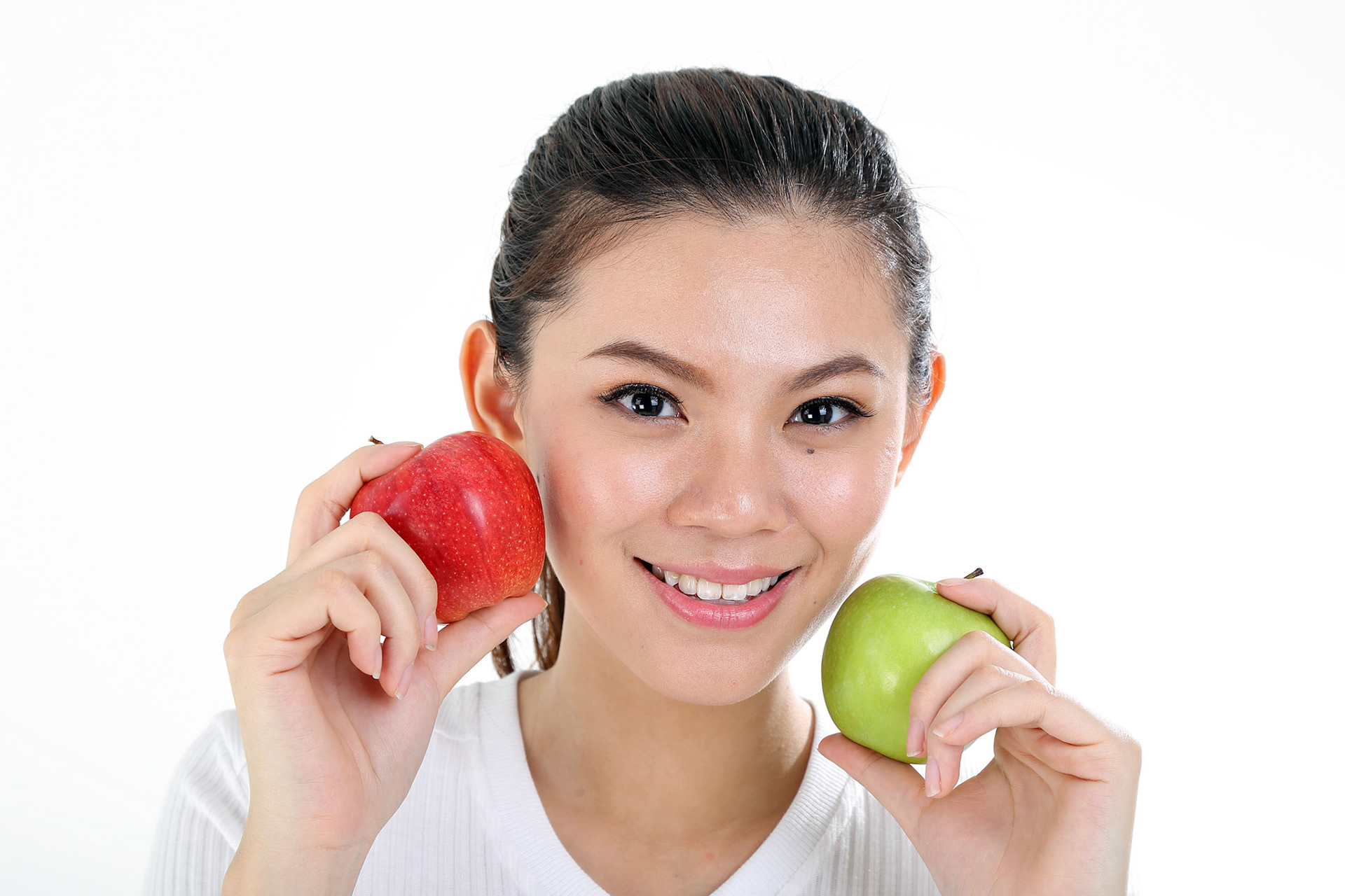 beautiful young south east Asian Chinese woman holding healthy green and red apple on cheek on white background