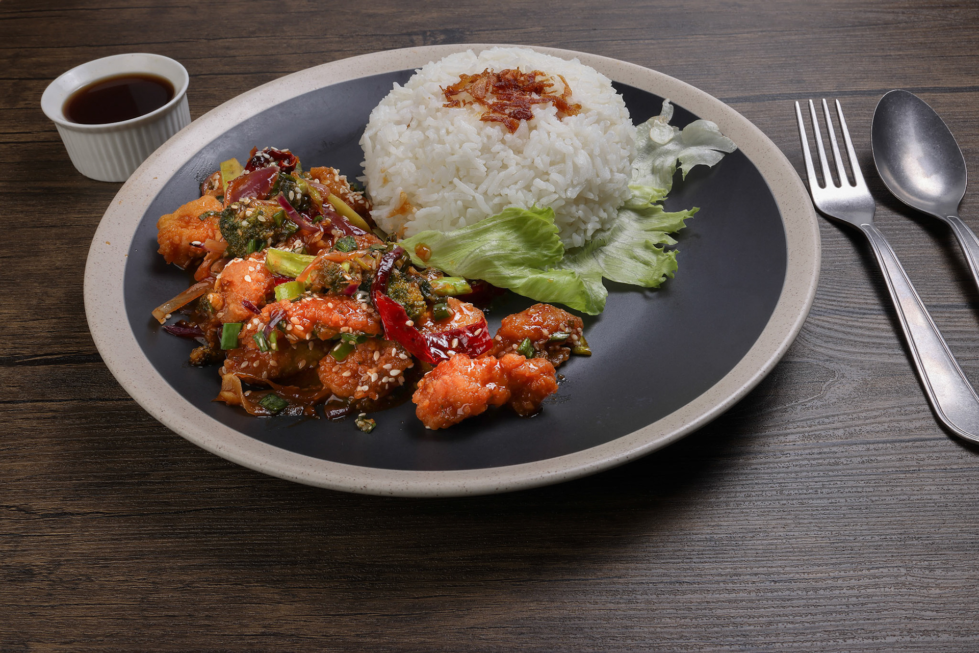 Chinese style Kung Pao Gong Bao Kung Po stair fried chicken with steamed rice lettuce on dark plate sauce fork spoon on rustic dark wood table
