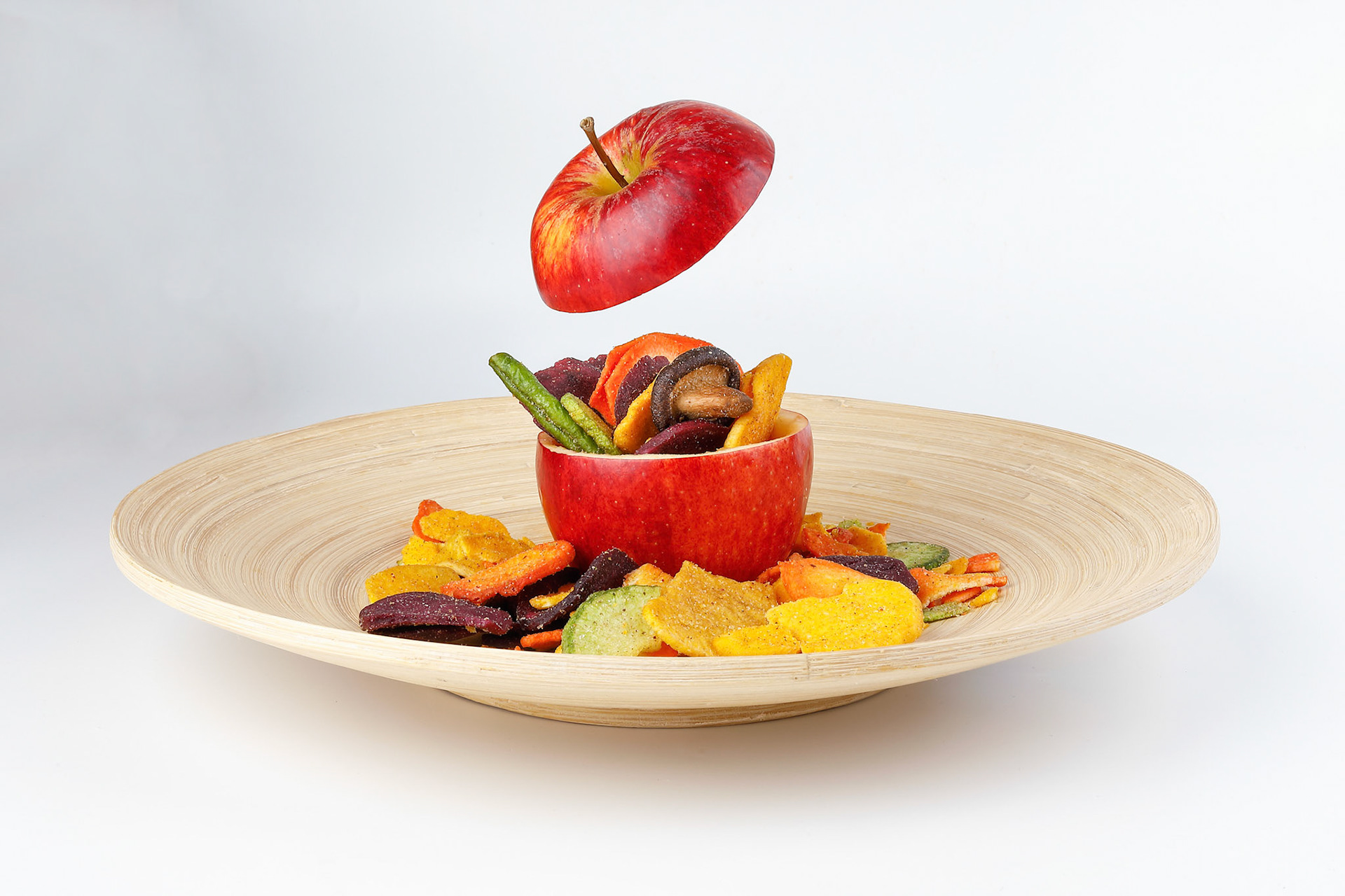 Healthy vegetable chips yellow sweet potato purple carrot green radish green beans and shiitake mushrooms in hollow red apple white background wooden plate