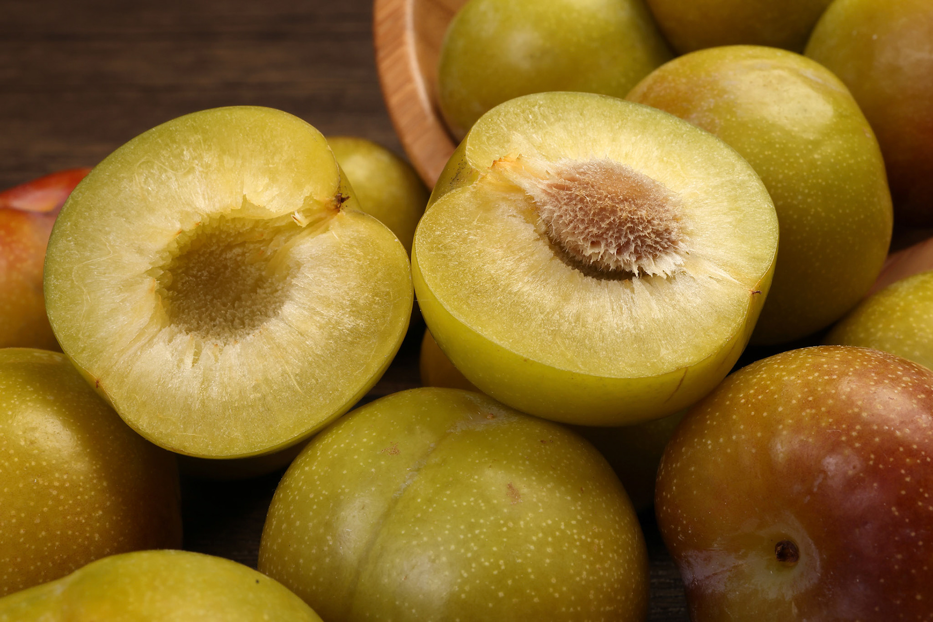 Ripe sweet small mini plum green maroon on rustic wooden table bowl black background