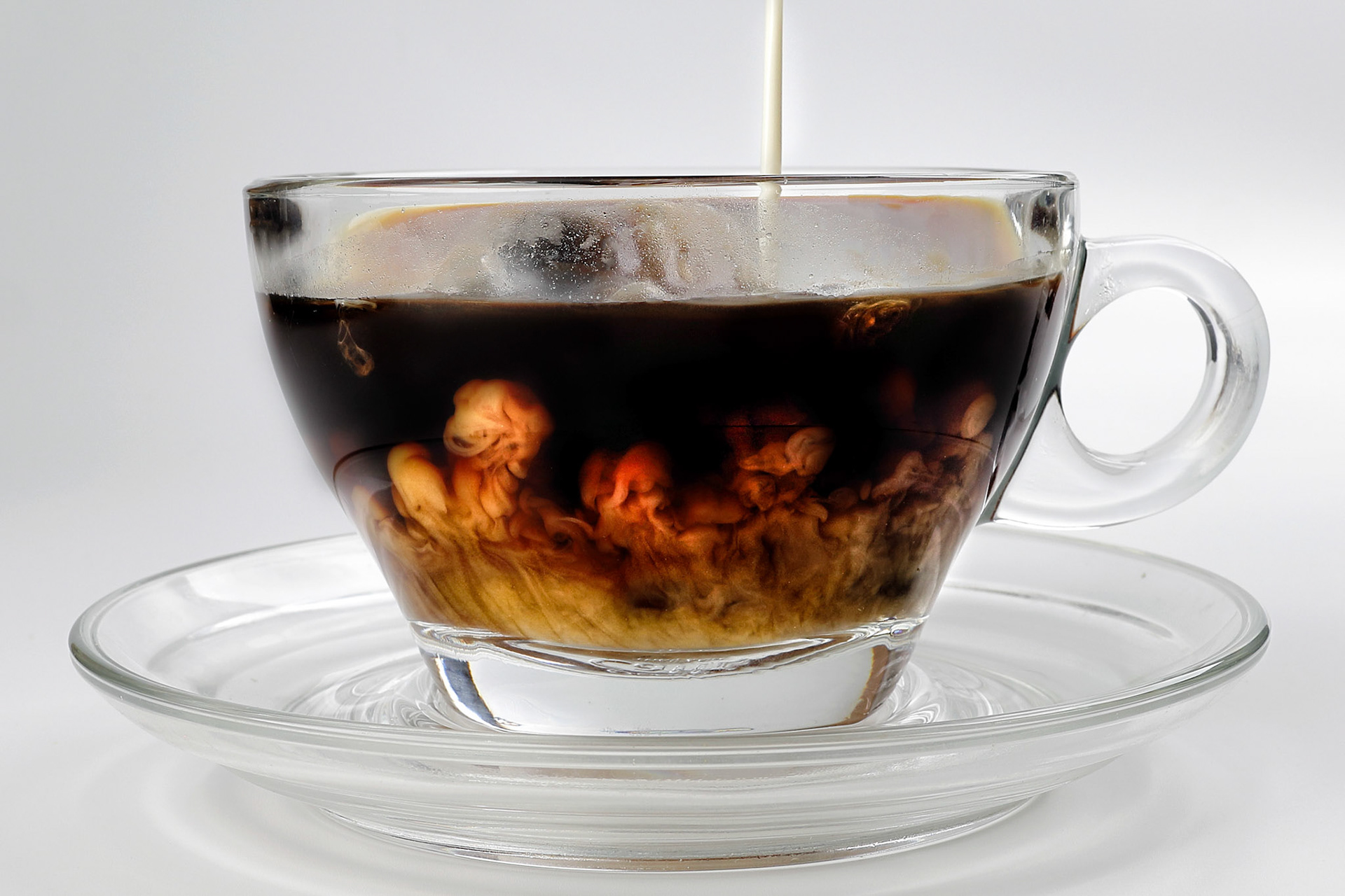 dark Coffee poring white milk dripping splash shadow liquid swirl in glass cup saucer on white background