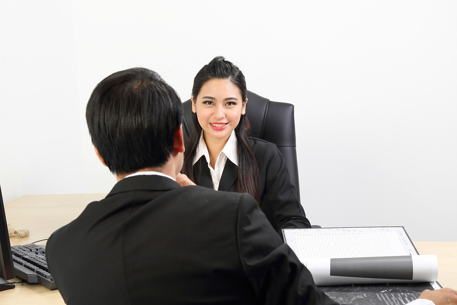 Young Asian male female wearing suit sitting at office desk look at camera over the shoulder