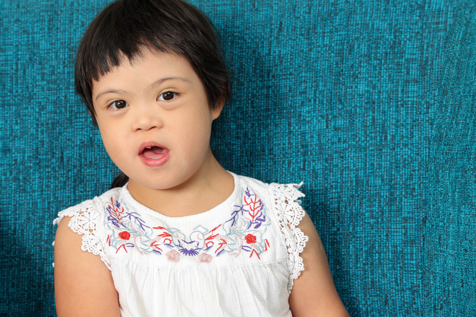 Portrait of southeast Asian small little girl child sitting on blue sofa look happy smile pose. She have down syndrome