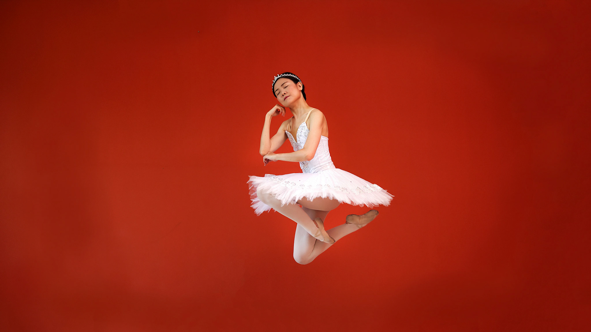 Beautiful Asian woman ballet dancer practice dance jump move wearing tutu at home red orange background wall