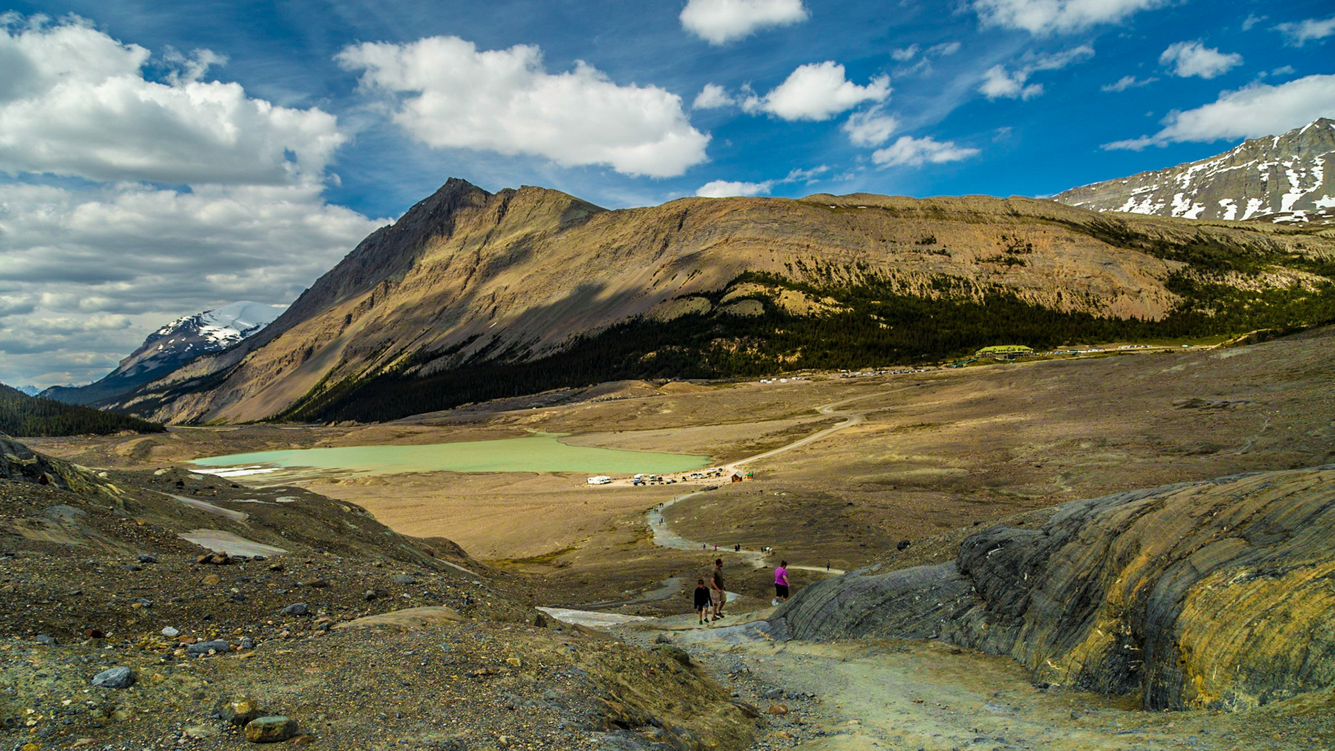 At the Columbia Icefield Discovery Centre, there are apparently some kind of vehicle tours that go onto the ice field.  We elected to take the dirt road to a parking lot by Sunwapta Lake and the hiking trail to a close viewing area for Athabasca Glacier.  It was a pretty good, rough climb onto the moraine left by the glacier as it has retreated toward for some time.  We loaded ourselves with considerable equipment.  When I reached the crest of the moraine, parking area, lake and mountains had an impressive scale, as I have attempted to capture in this image.