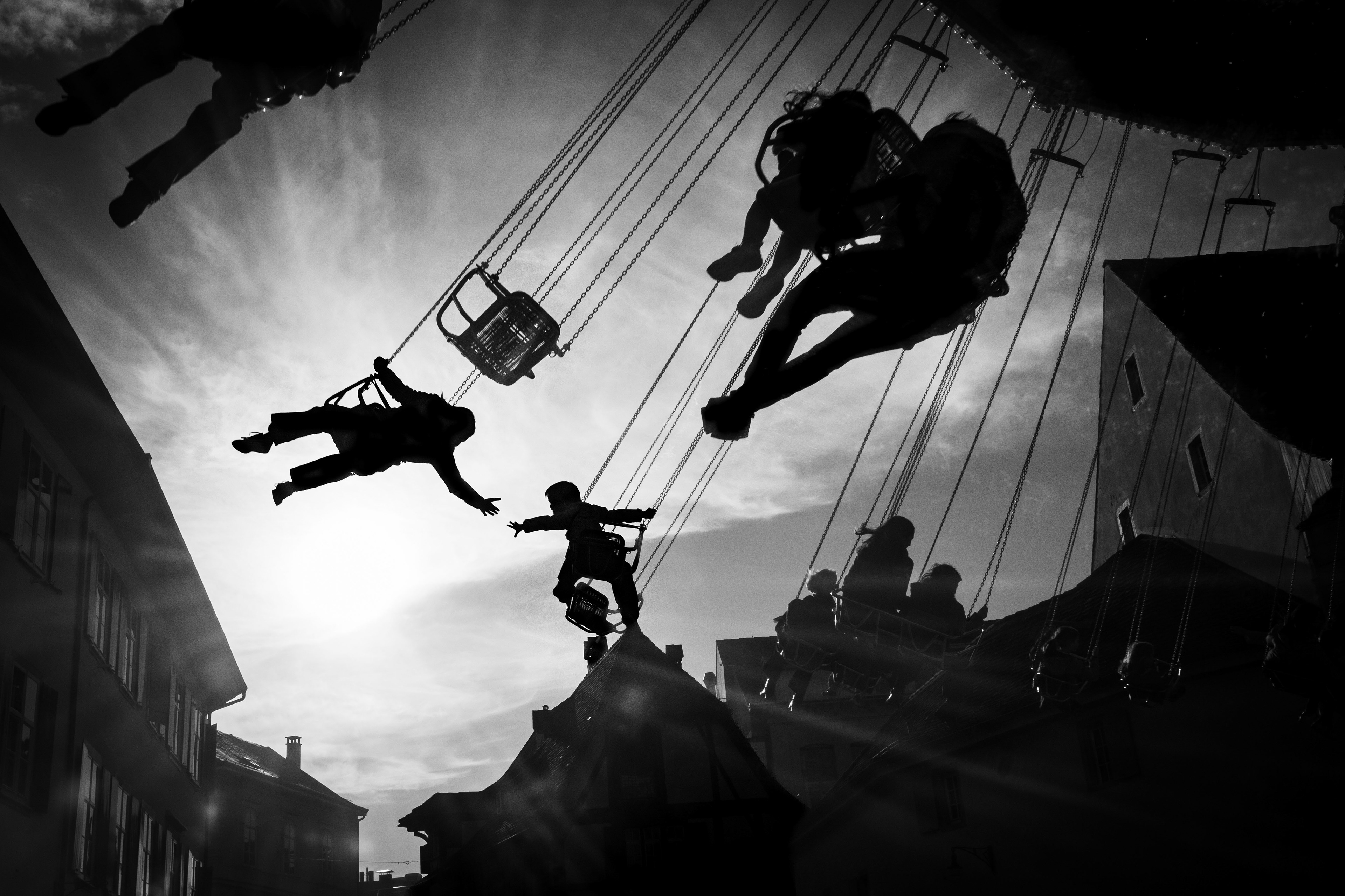 Black & White Reaching Across the Sky Two children high above the Basel Herbstmesse reach out and hold hands in mid-air. Photography by Carmine Castelli