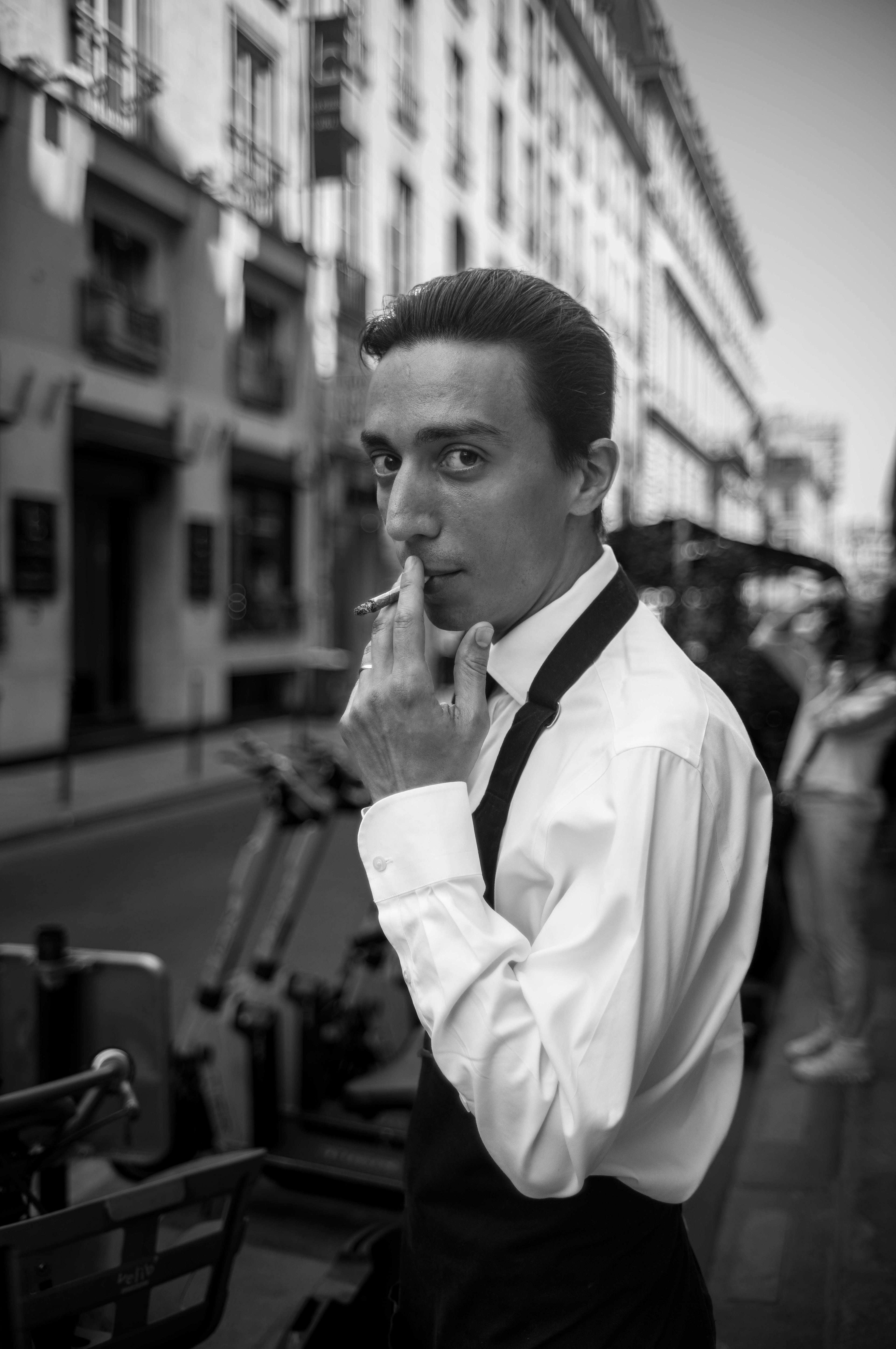 Candid B&W street photo: a 1960s-style waiter smoking a cigarette in Paris. Photography by Carmine Castelli