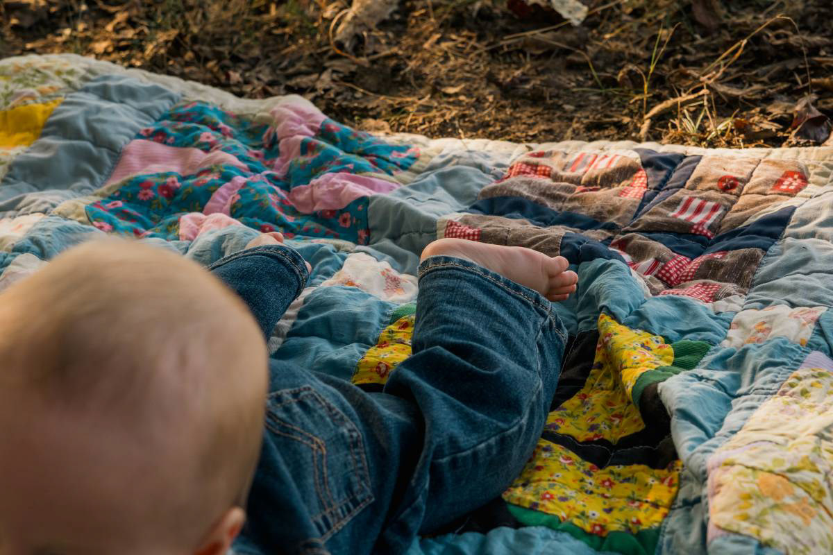 Candid outdoor baby photoshoot details, showing a baby laying on a quilt in a natural setting.