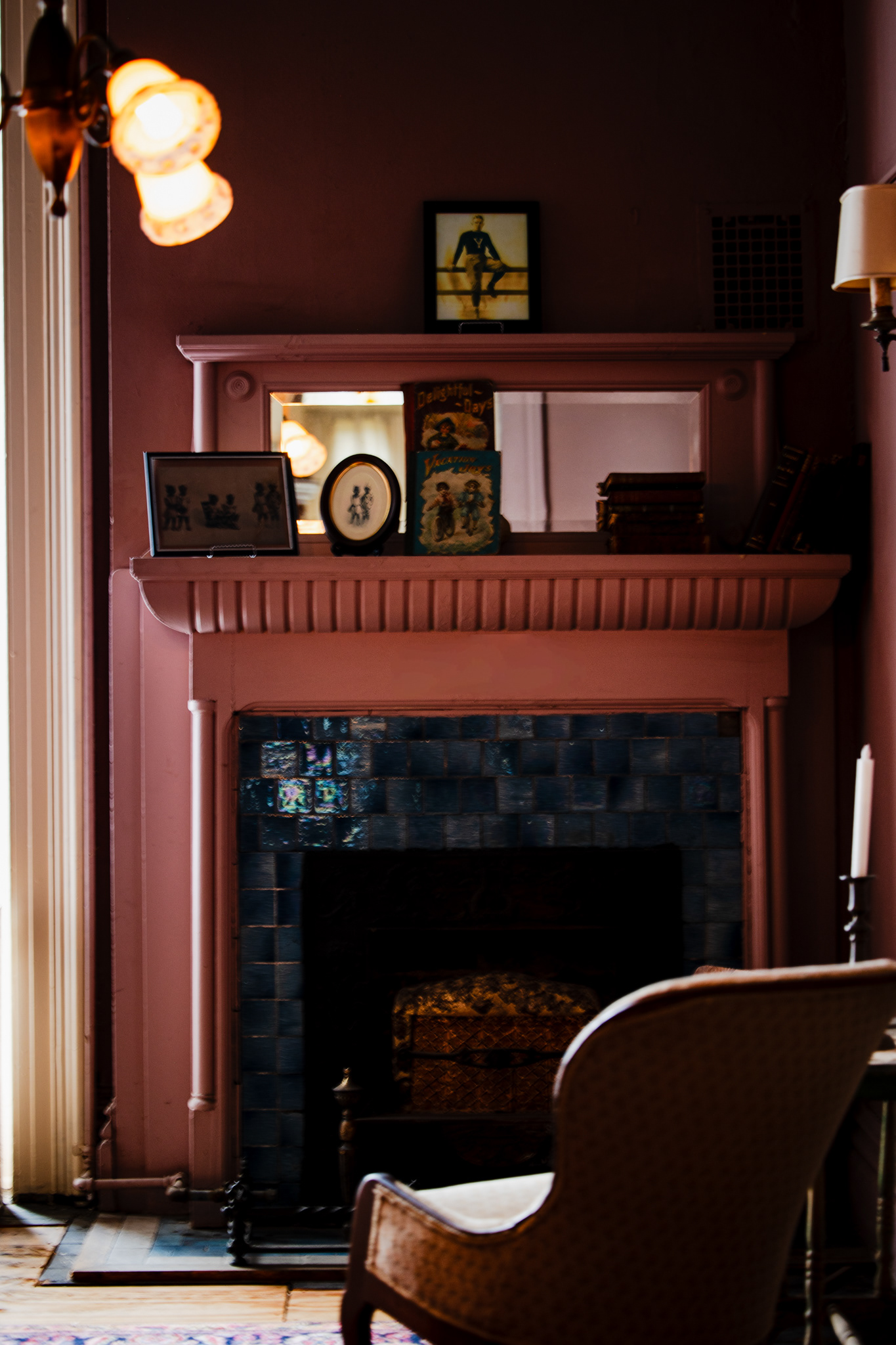Pink-painted fireplace mantel with antique books and framed photographs at the Mallory- Neely House, Memphis, TN