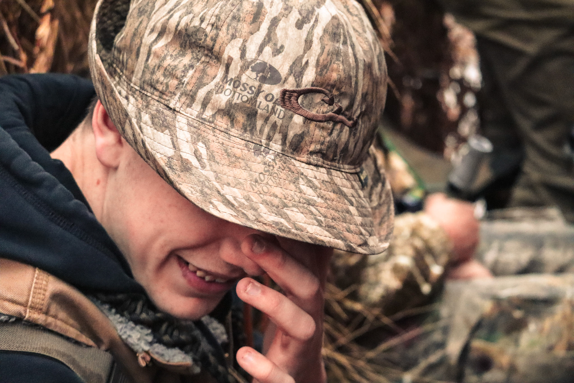 A waterfowl hunter wearing a camouflage hat and jacket uses a duck call in the flooded timber of the Arkansas Delta.