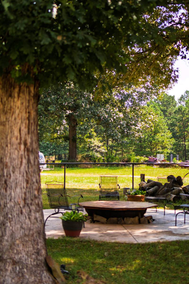 The ultimate outdoor living space for cool evenings. A dedicated fire pit area surrounded by mature trees offers guests the perfect spot to unwind and take in the natural surroundings. Outdoor area of Air Bnb captured by Arkansas photographer.