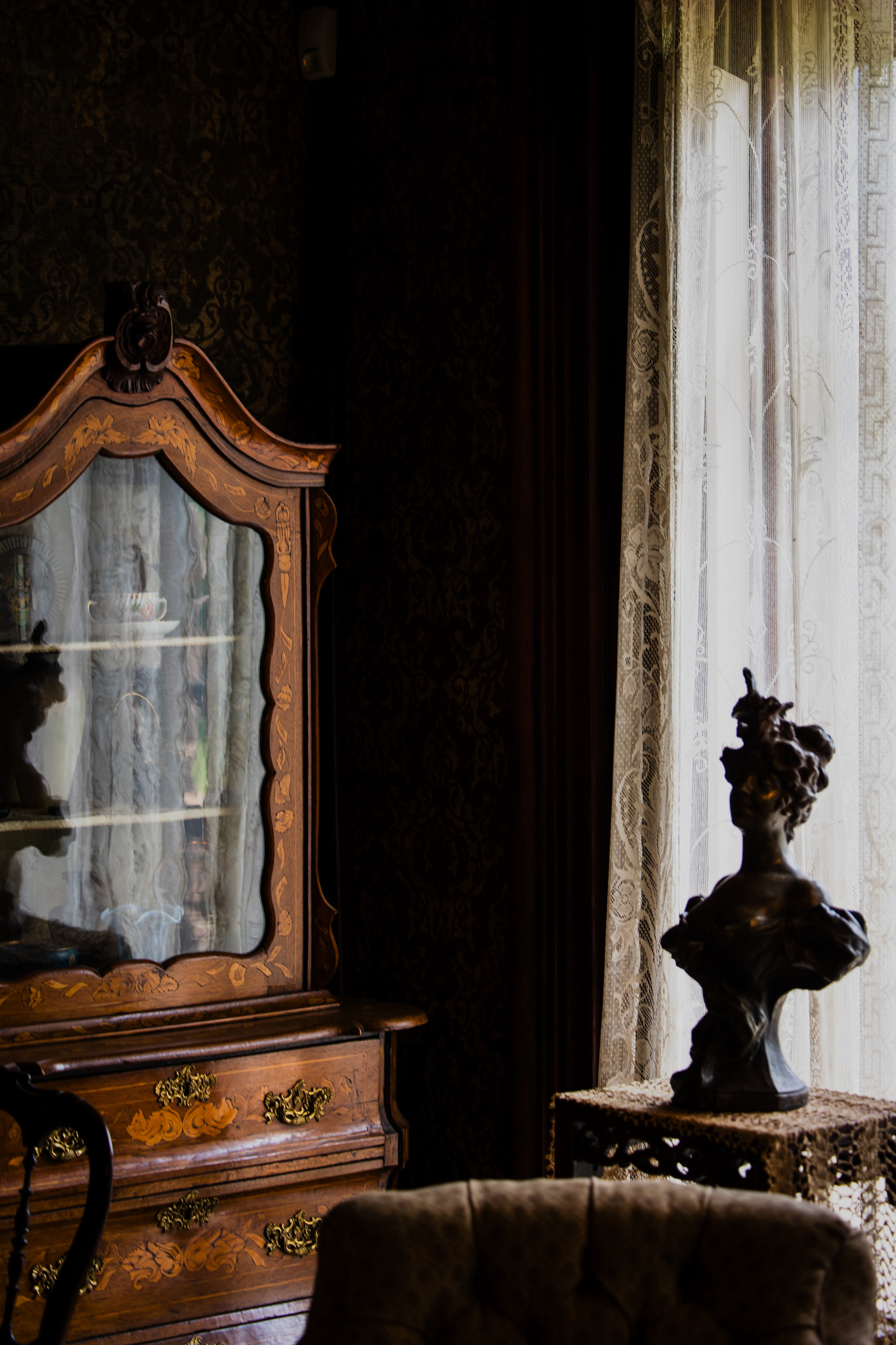 Antique marquetry mirror cabinet and bronze bust on a lace-draped pedestal in a parlor at the Mallory-Neely House, Memphis