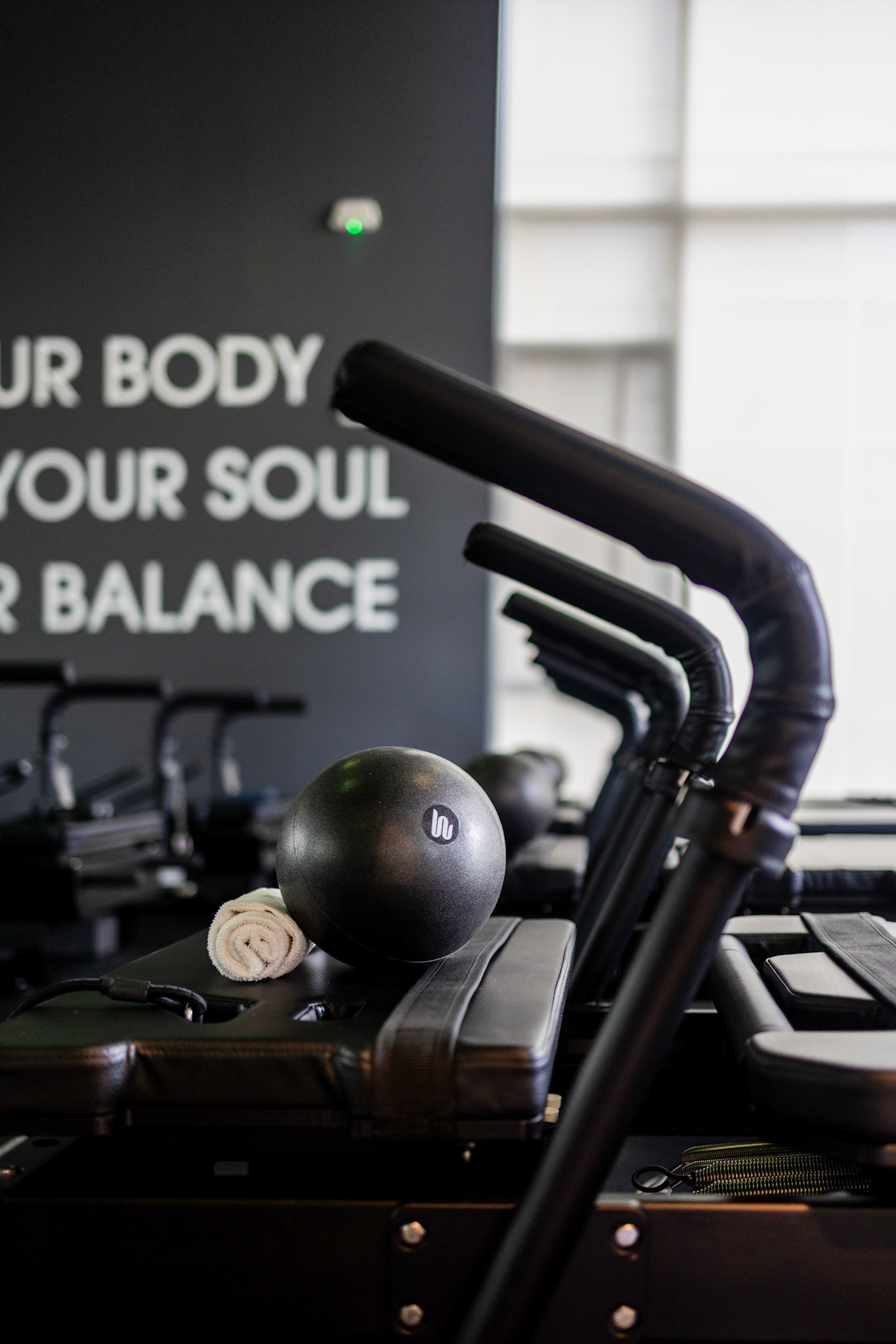 Close-up of a black weighted ball and rolled white towel resting on a Pilates reformer carriage, showcasing atmospheric Northwest Arkansas brand photography inside a modern fitness studio.