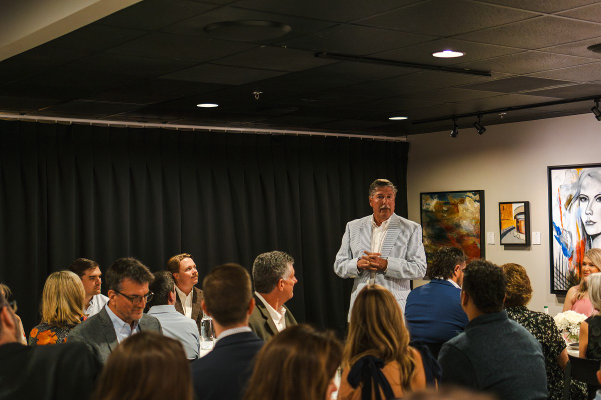 Candid indoor rehearsal dinner photography in Rogers, AR of a guest speaker addressing an audience at an art gallery venue.