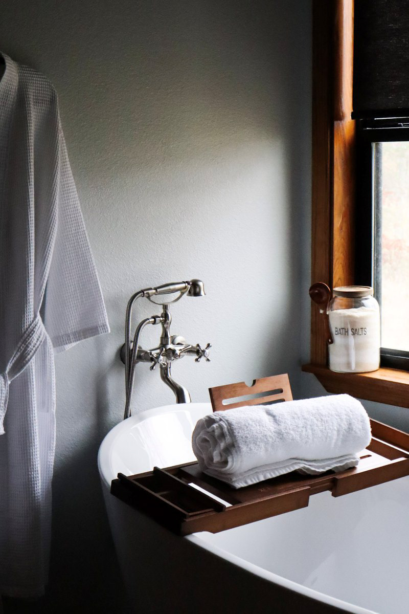 Creating a spa-like retreat for guests. Essential short-term rental amenities like this deep soaking tub, styled with a wooden bath tray, fresh linens, and a cozy robe, make all the difference for a relaxing getaway. Boutique vacation rental, short-term rental photography, spa bathroom, Airbnb amenities, Bauxite Arkansas stays.