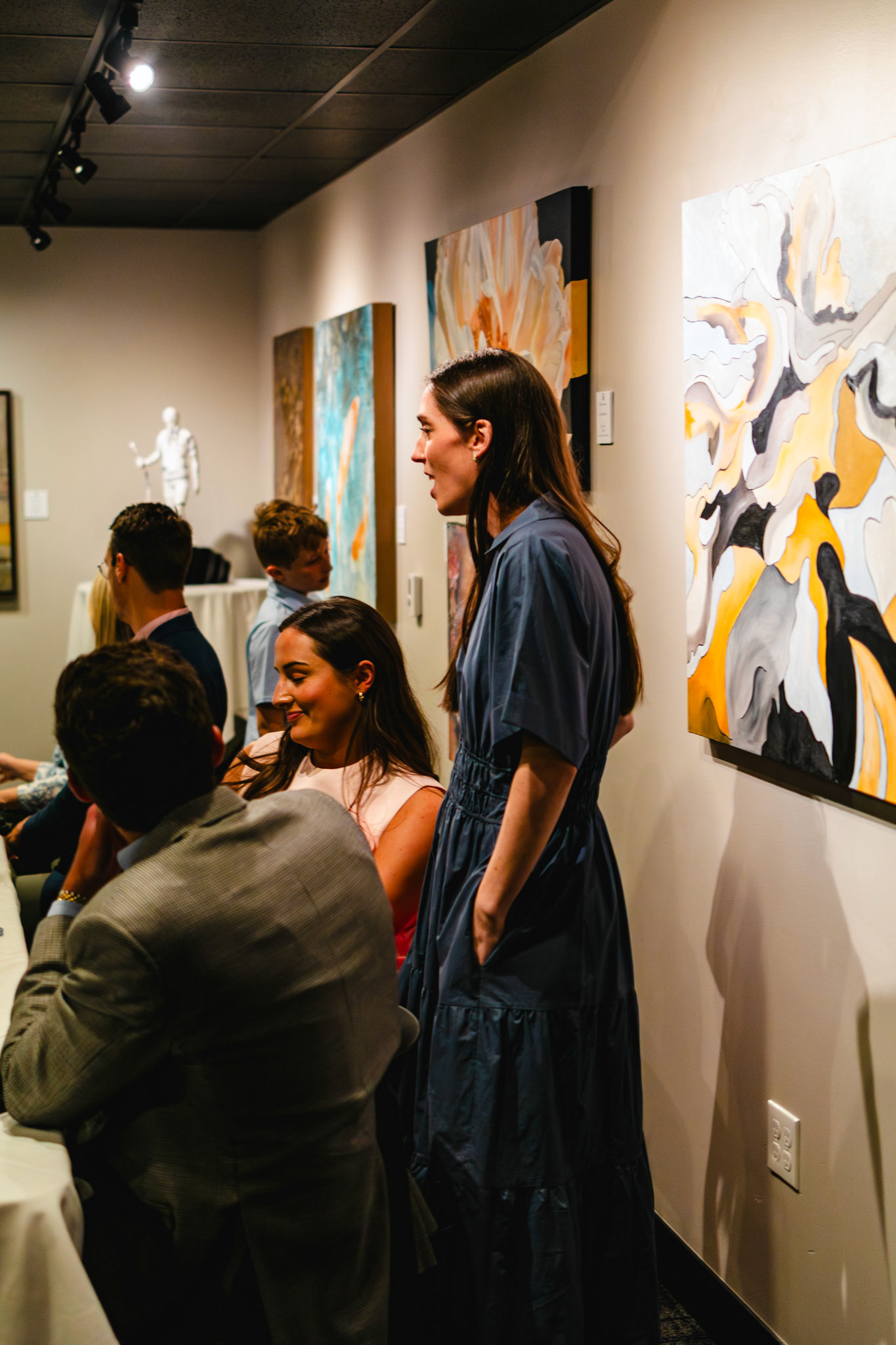 A woman in a blue dress stands and mingles with seated guests during an intimate event at Theos in Pinnacle Hills.