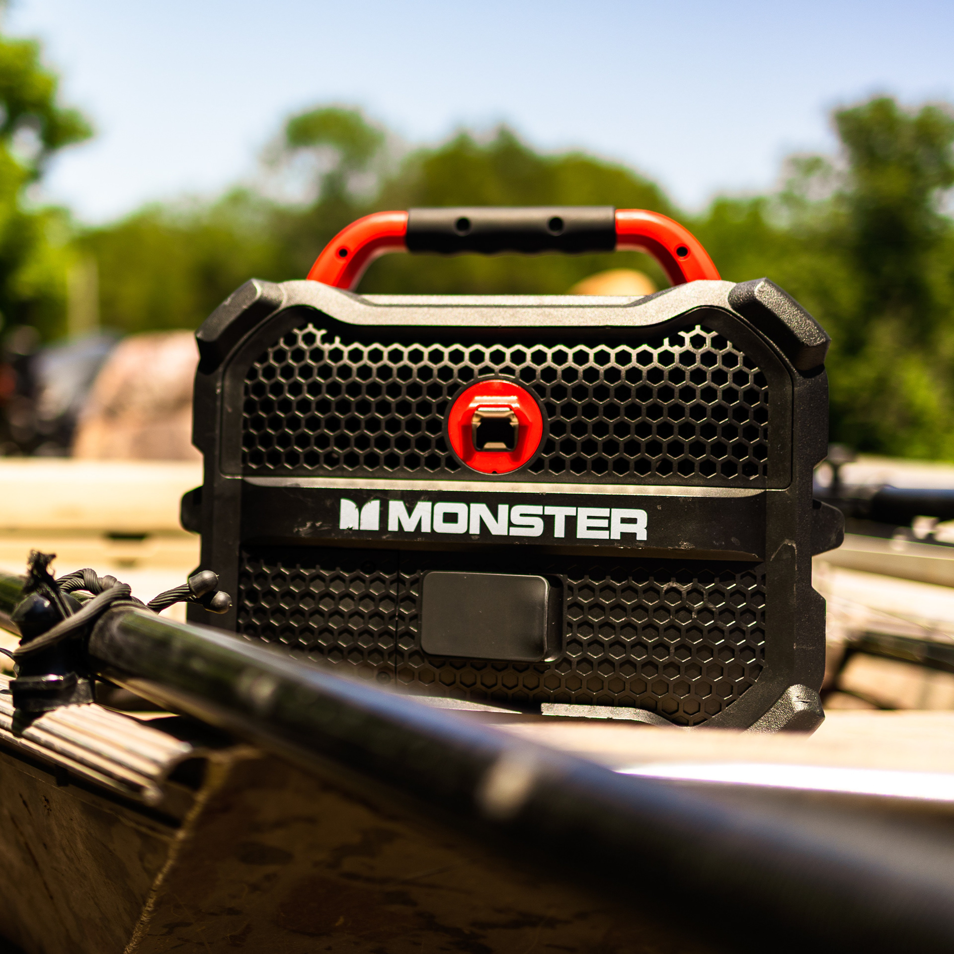 Close-up of a rugged Monster BamBox speaker resting on a boat edge during an Arkansas commercial product photography shoot, featuring natural outdoor lighting and a soft-focus nature background
