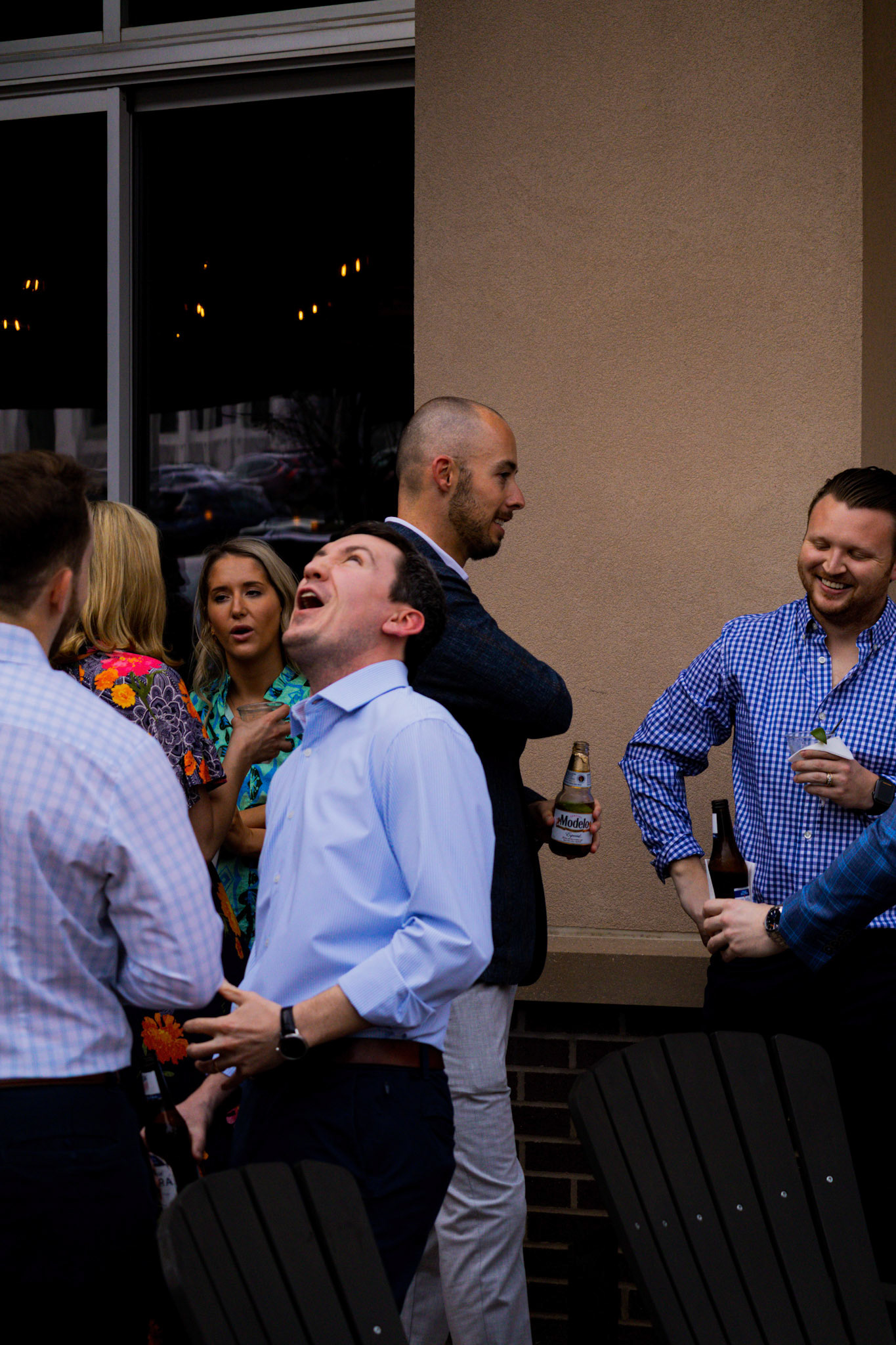 A candid photograph of guests laughing together on the outdoor patio during a rehearsal dinner celebration in Rogers, Arkansas.