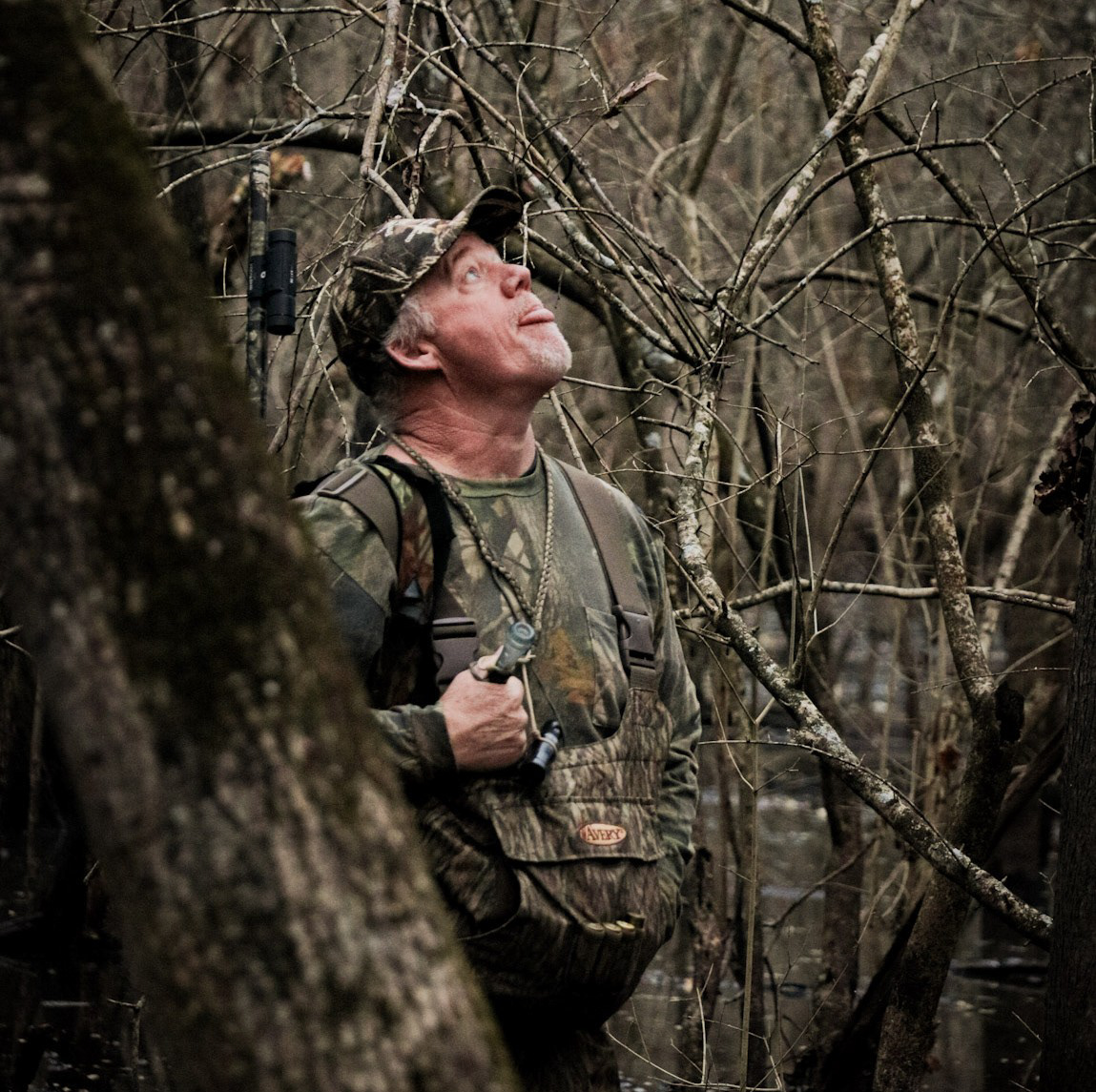 A hunter in camouflage looks up into the canopy of flooded timber during an early morning duck hunt