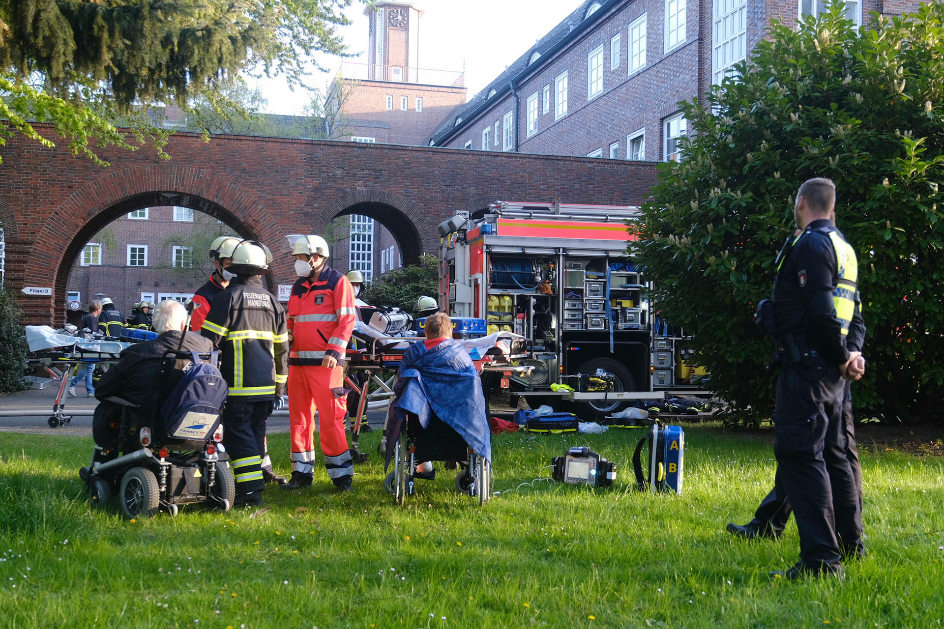 Großeinsatz der Feuerwehr Hamburg mit rund 200 Einsatzkräften am Dienstag. Im von Fritz Schumacher entworfenen historischen Pflegeheim Groß Borstel, in dem heute Fördern & Wohnen 115 betreute Wohnungen für Senioren und Pflegebedürftige betreibt, war am frühen Abend ein Brand ausgebrochen, bei dem insgesamt 14 Menschen verletzt wurden. Zwei von ihnen erlitten so schwere Verletzungen, dass sie in Lebensgefahr schweben. 170 Menschen leben in der Anlage, alle mussten am Dienstag mindestens kurzzeitig ihre Wohnungen verlassen. Das Feuer war in einer der Wohnungen im ersten Obergeschoss ausgebrochen, der Brandrauch zog jedoch, schnell über das zweite Obergeschoss bis ins Dach des Gebäudetraktes. Wegen des sich schnell ausbreitenden Rauchs und um für die Sicherheit der Bewohner zu sorgen wurde aber die gesamte Anlage evakuiert. Der Gebäudeteil, in dem die Brandwohnung liegt, ist vorerst unbewohnbar. Fördern & Wohnen bemüht sich um die anderweitige Unterbringung der Betroffenen. Um sowohl die Menschenrettung als auch die Brandbekämpfung gewährleisten zu können, wurde eine außergewöhnlich große Zahl von Einsatzkräften zusammengezogen. Die Borsteler Chaussee und die angrenzende Papenreye standen voll mit Einsatzfahrzeugen, darunter ein Großraumrettungswagen. Auch die Polizei war mit vielen Beamten aus dem ganzen Stadtgebiet vor Ort, unter anderem mit einem Zug der Bereitschaftspolizei. Ein Großteil der Einsatzkräfte kümmerte sich um die Versorgung der geretteten Anwohner. 14 Menschen wurden verletzt, fünf von ihnen leicht. Unter den neun Schwerverletzten sind zwei Fälle mit lebensbedrohlichen Verletzungen. Aber auch viele der der oftmals gebrechlichen und gesundheitlich eingeschränkten Menschen, die unverletzt blieben, brauchten zumindest vorübergehend Betreuung und Ansprechpartner.