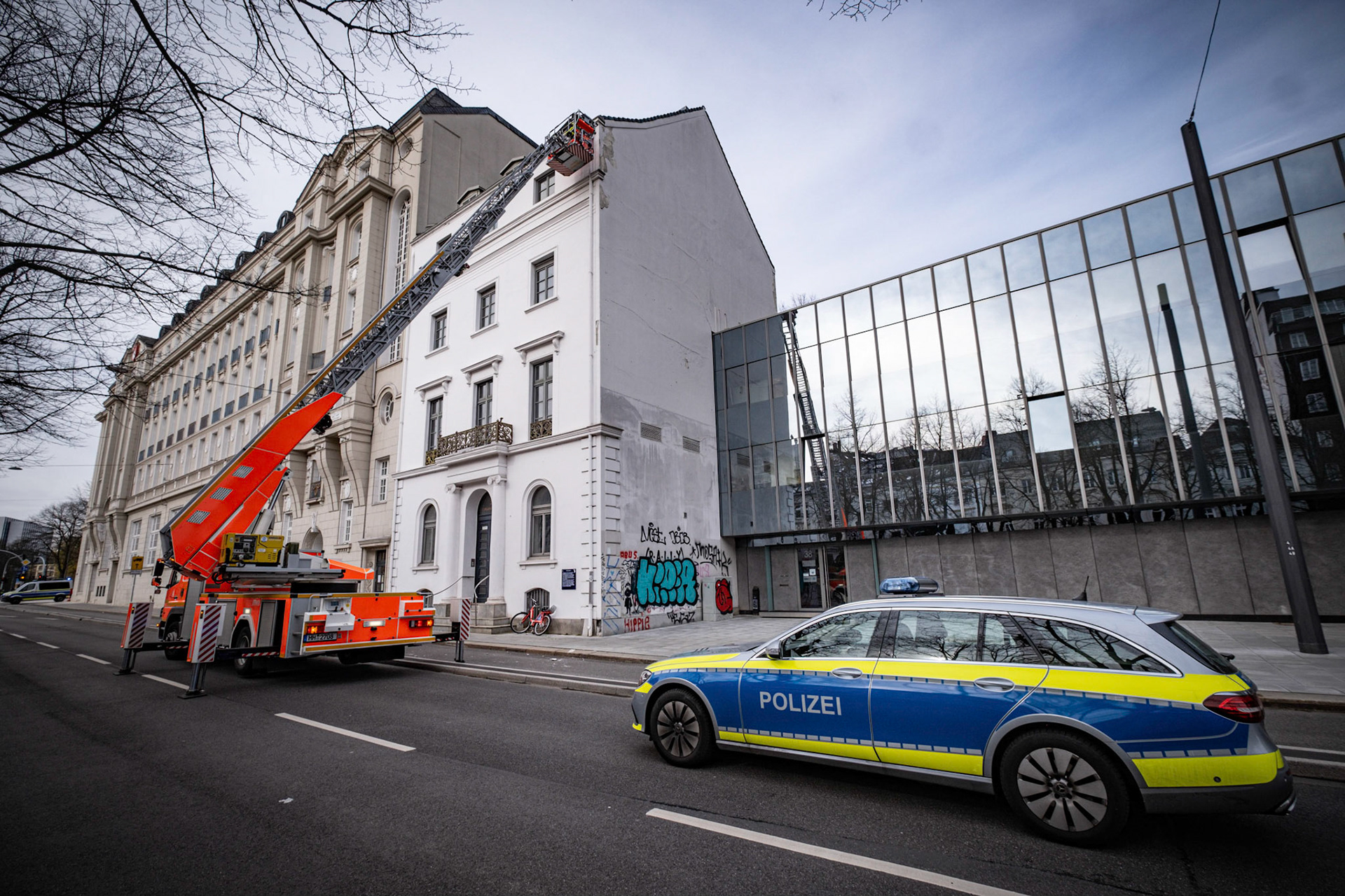 Am Mittwochmittag musste die Polizei die Esplanade sperren. Der Verkehr staute sich bis zum Wallringtunnel. Teile einer Hausfassade sind auf den Radweg und die Straße gestürzt. Die Feuerwehr rückte mit einer Drehleiter an. Ein Feuerwehrmann überprüfte die Fassade und entfernte weitere lose Teile der Fassade. Polizisten sperrten im Anschluss den Fuß- und Radweg mit Flatterband. Nun muss der Hauseigentümer die Fassade von einer Fachfirma überprüfen und reparieren lassen, damit es mit zu weiteren abstürzen kommen kann.