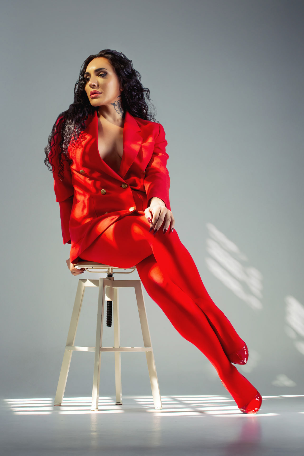 Model in a red suit on a stool, geometric window light. Book session in Barcelona by Alberto Branca