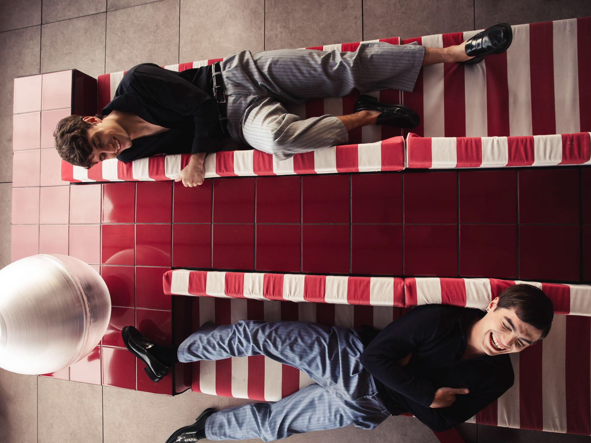Overhead view of two men on a red and white striped floor, one lying and one seated, Euphoria, photographed by Alberto Branca