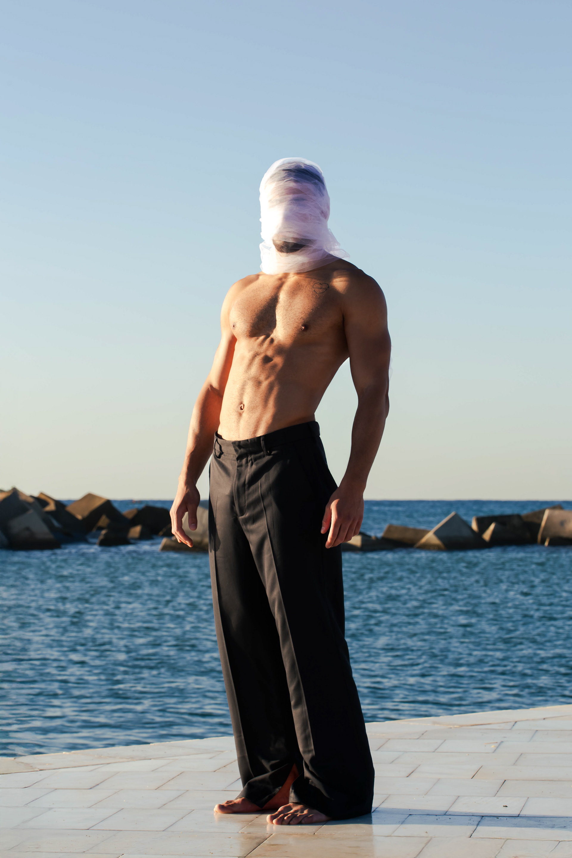 Model in black trousers with a white veil over his head, For All Those About to Rock, photographed by Alberto Branca