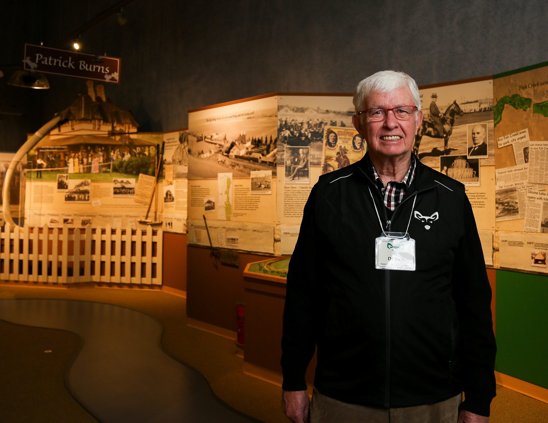 Dennis Burns poses for a photo in front of the Senator Patrick Burns exhibit in the visitor centre at Fish Creek Provincial Park in Calgary on Thursday, Feb. 17, 2022. Burns volunteers at the visitor centre with Friends of Fish Creek. He brings a unique perspective, as he lived at Bow Valley Ranch in Fish Creek for 20 years.