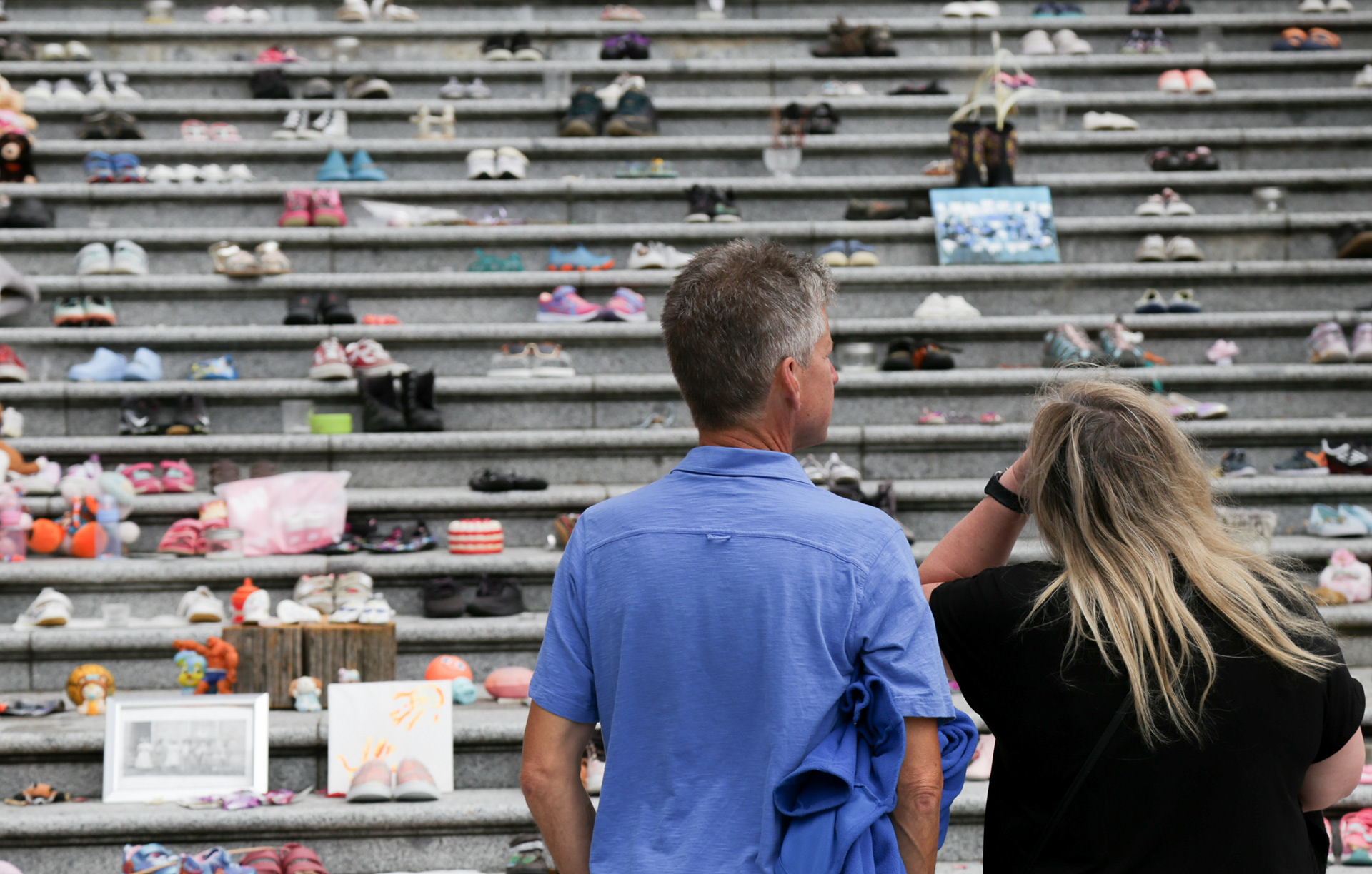 A couple looks at the hundreds of shoes that are a part of the memorial on the steps of the Vancouver Art Gallery in Vancouver on Saturday, July 17, 2021. Haida artist Tamara Bell designed the memorial with 215 children's shoes in May 2021. Bell made the memorial after 215 unmarked graves were found at the Kamloops Indian Residential School.