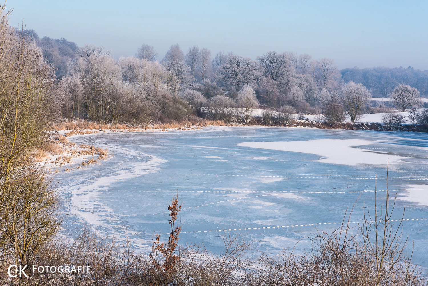 Zugefrorener See mit Bäumen im Rauhreif