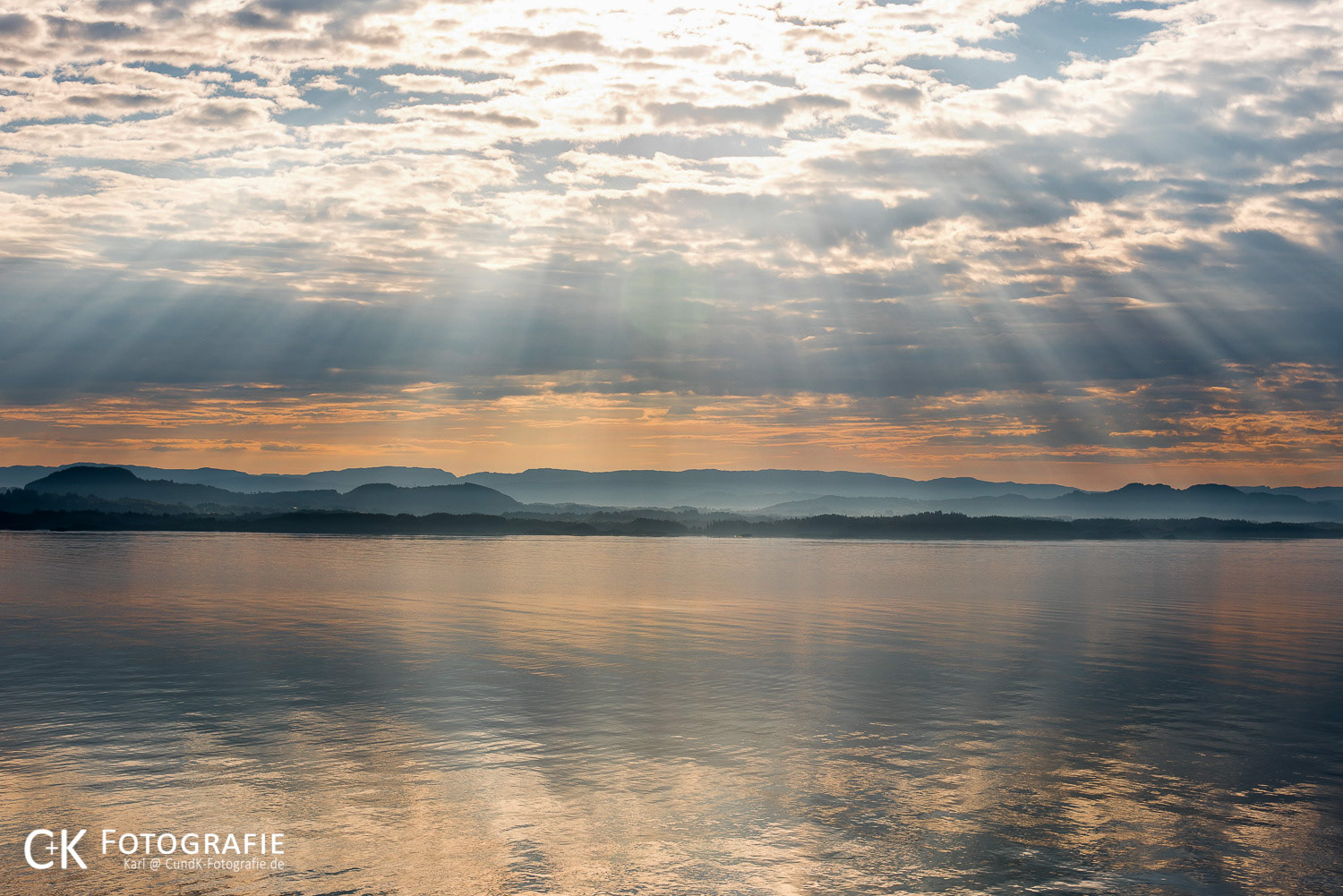 Morgenrot mit Wolken und Sonnenstrahlen im Fjord bei Bergen