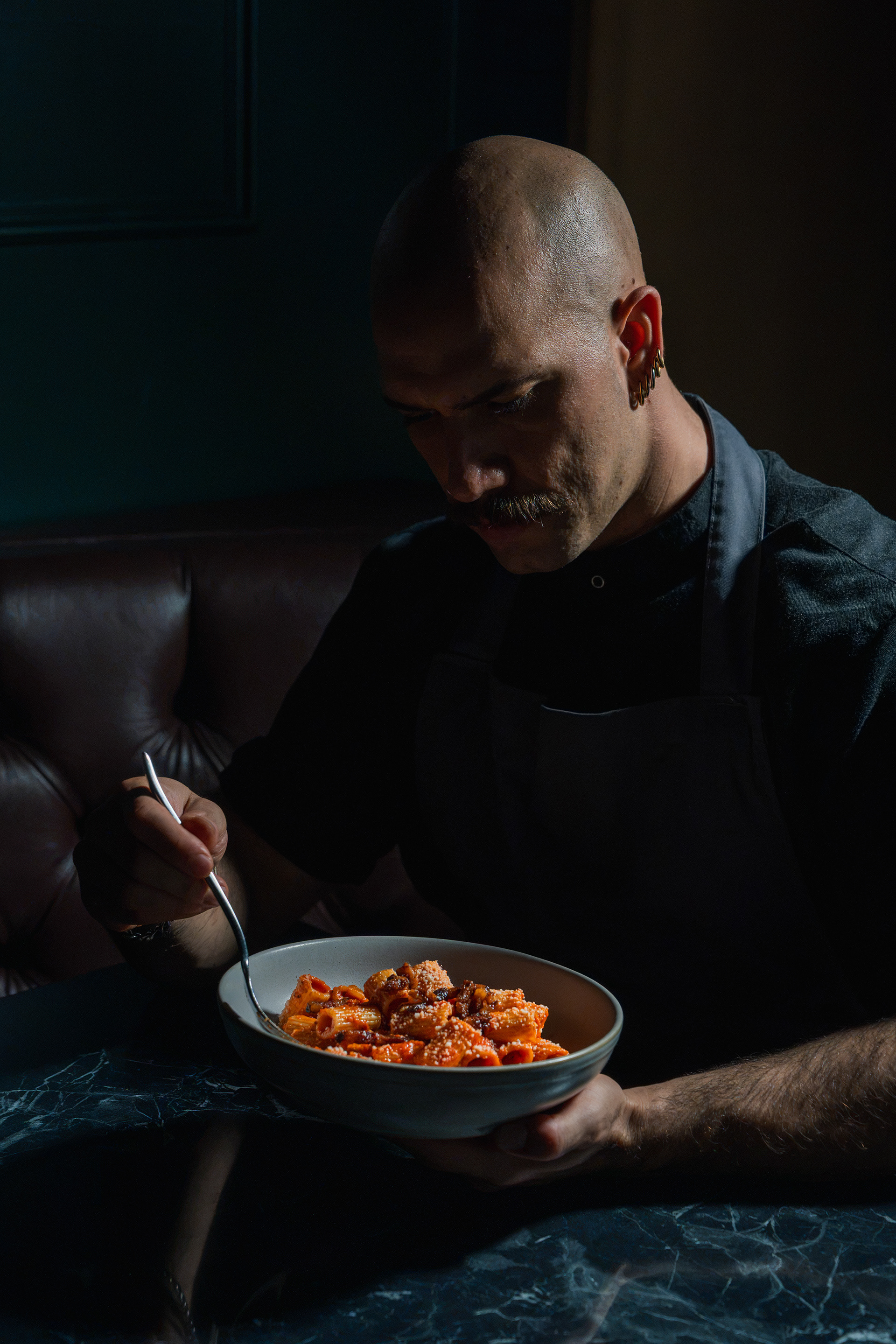 A man holding a bowl of pasta at Piano Piano, photographed in warm, low light.