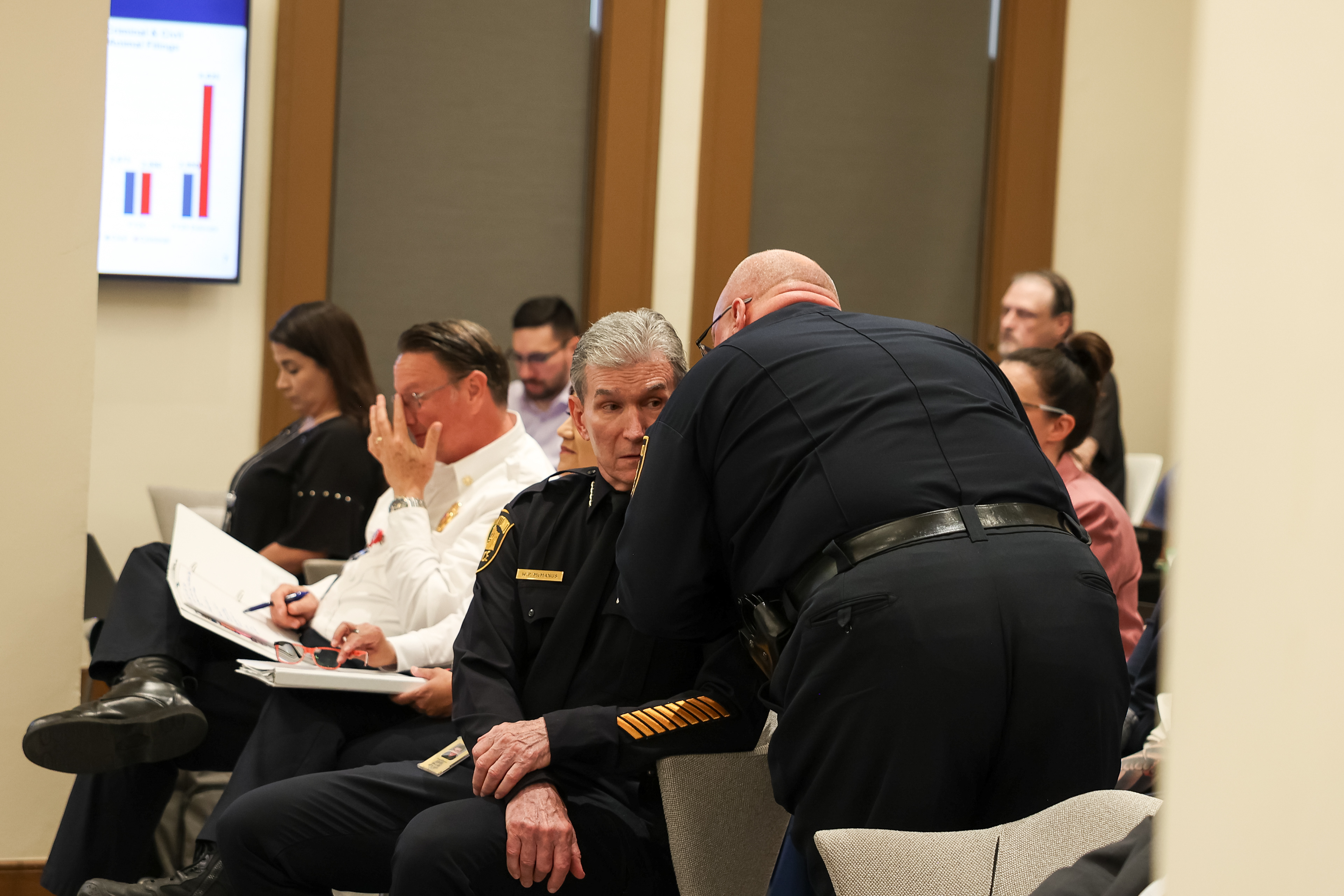 A San Antonio police officer whispers into Police Chief William McManus’ ear during a city budget work session on public safety on Aug. 19, 2025, in San Antonio.