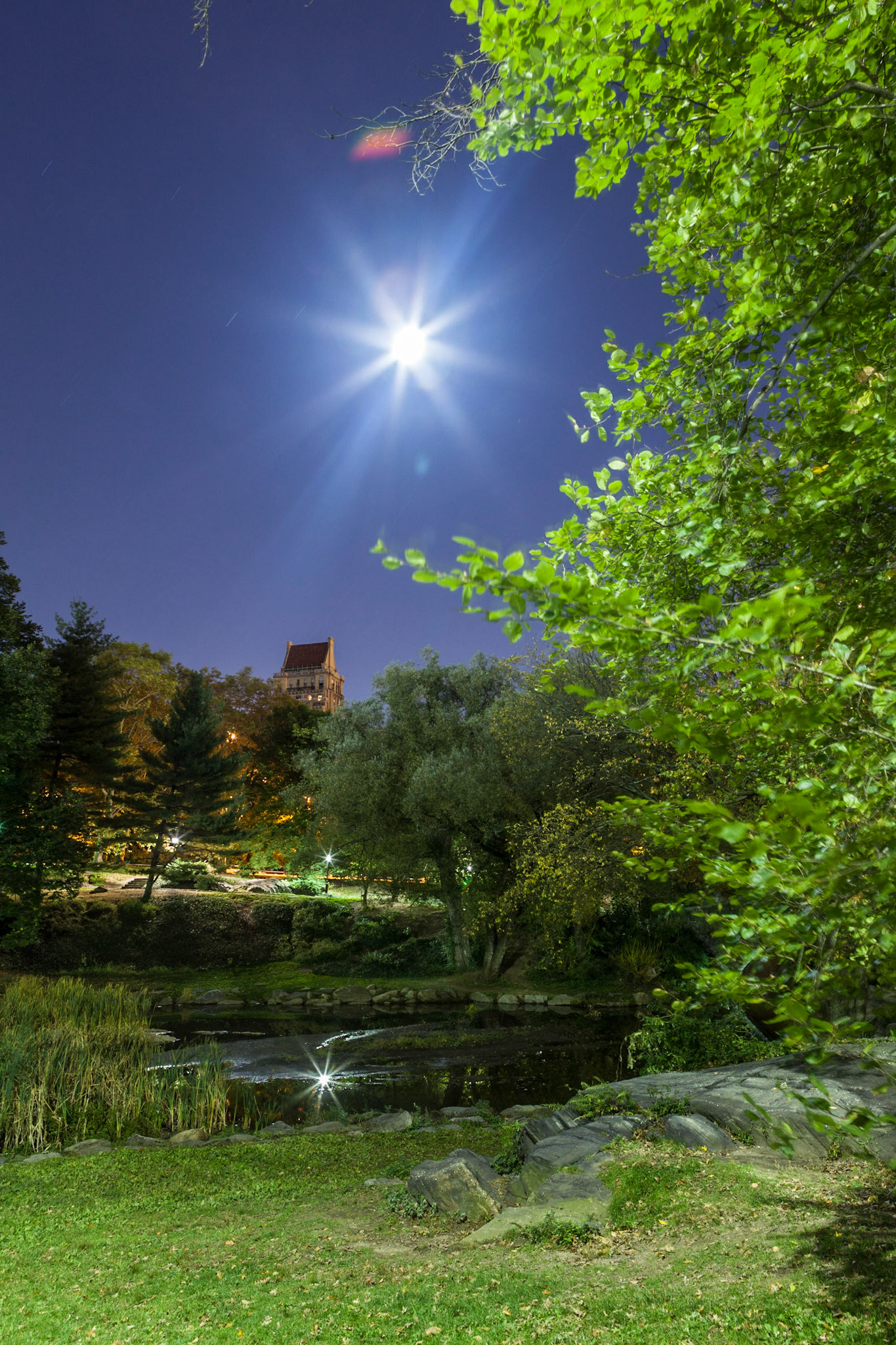 The night photography image was taken from a meadow above "The Pond" in the southern section of Central Park. The full moon over the Upper East Side reflects nicely in the lake.