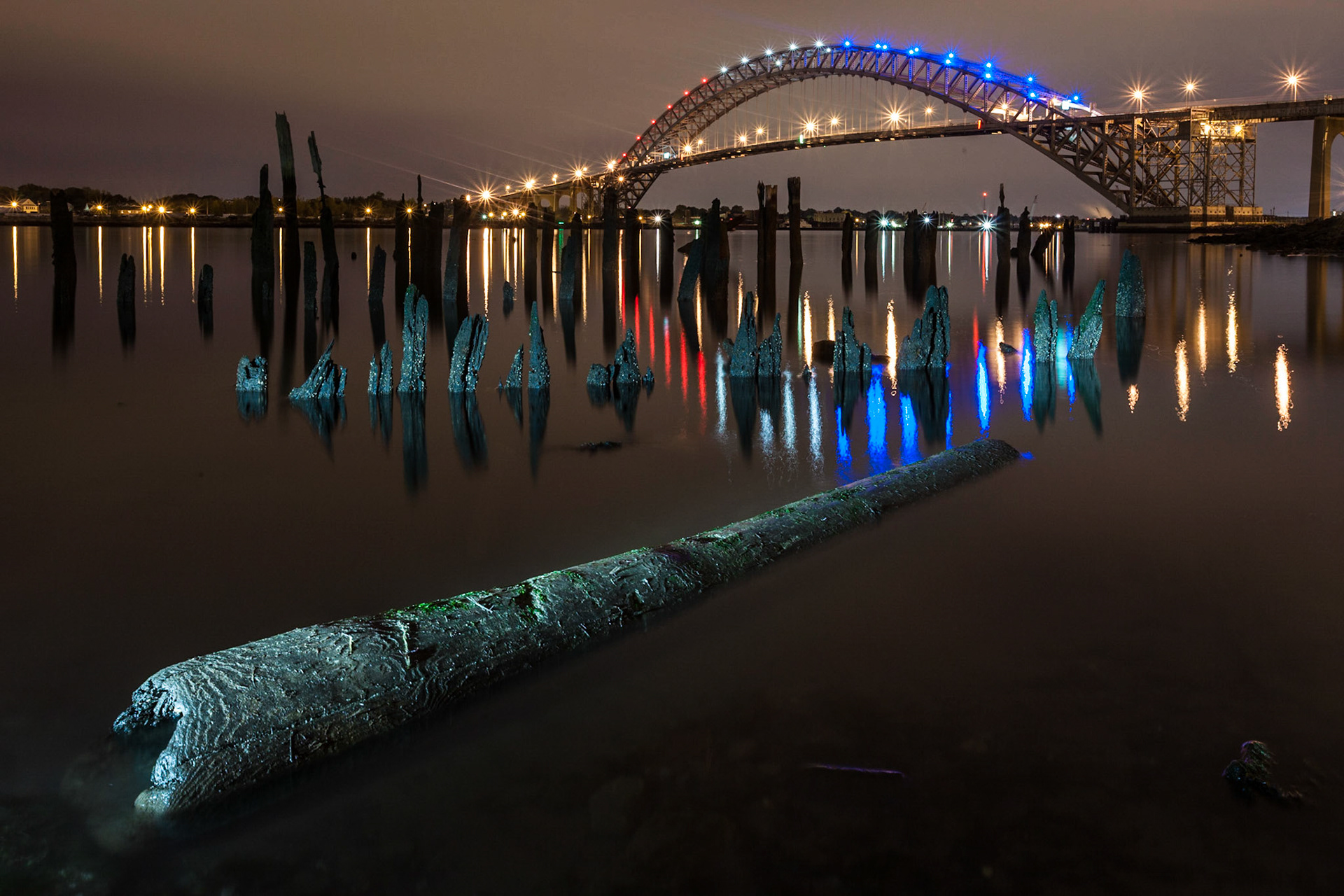 A night time image of the Bayonne Bridge from the northern shore in New Jersey. I really like the lit up log in the foreground together with the reflections and the poles of an old pier