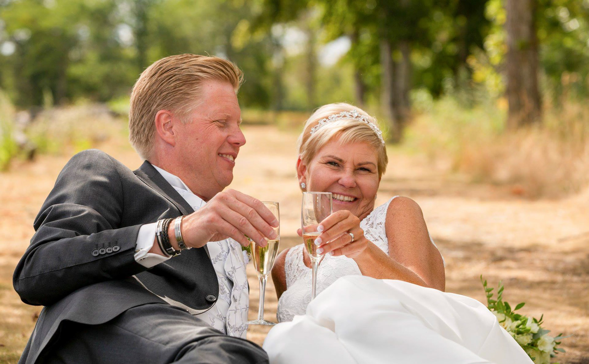 Ett gift par ligger på en väg i skogen och skålar champagne