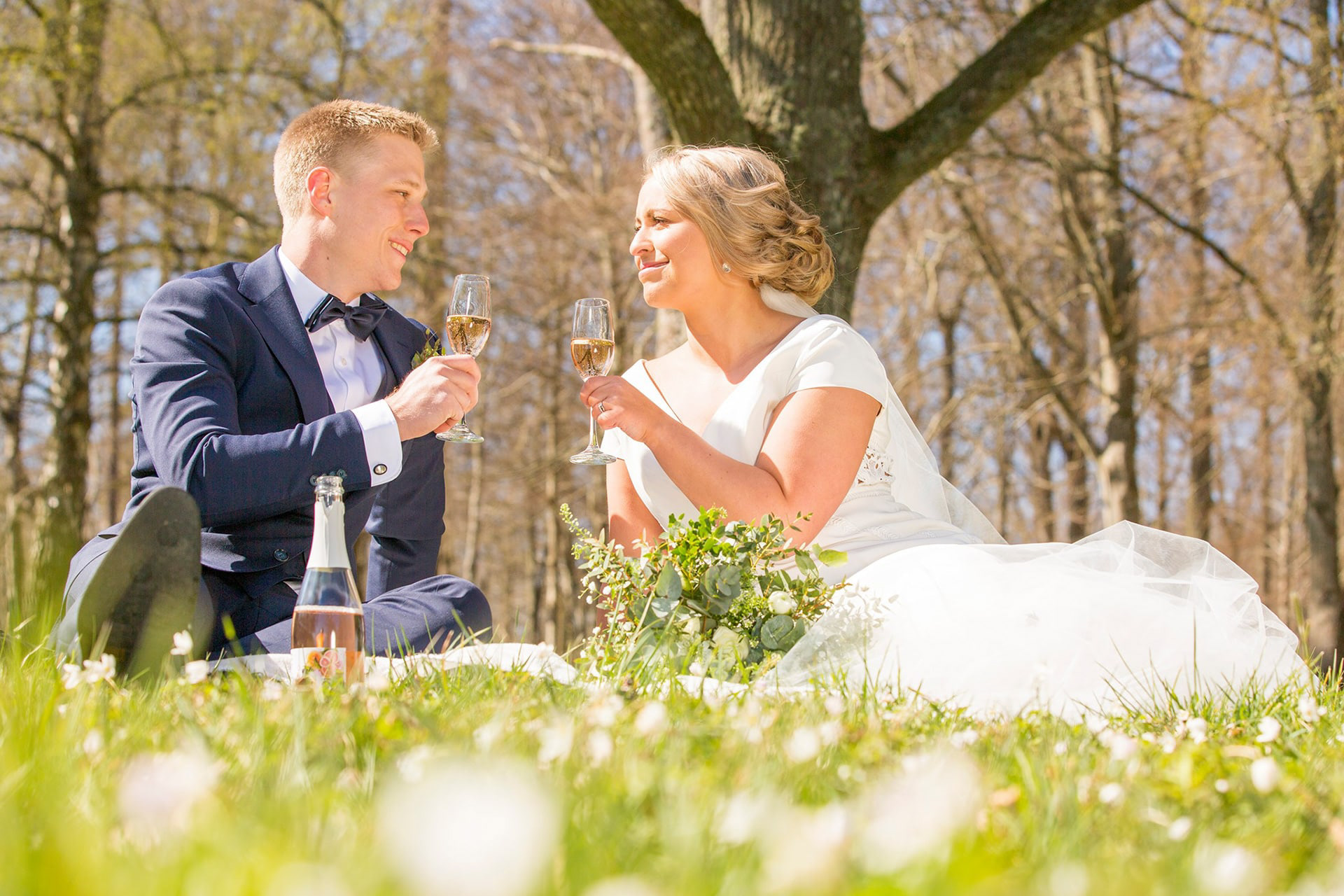 Ett brudpar skålar champagne med varandra i skogen