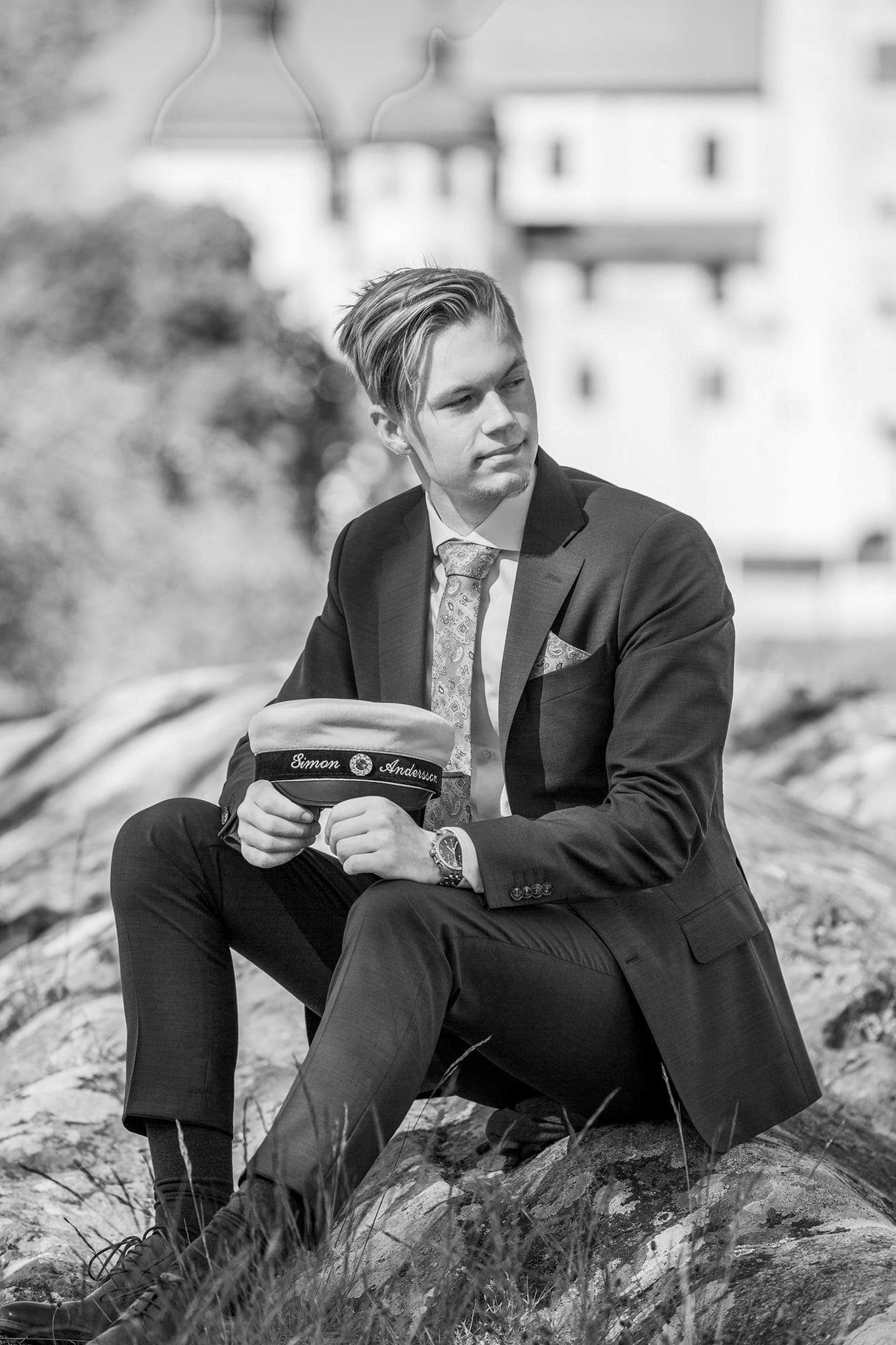 En student sitter på ett berg och håller i sin studentmössa