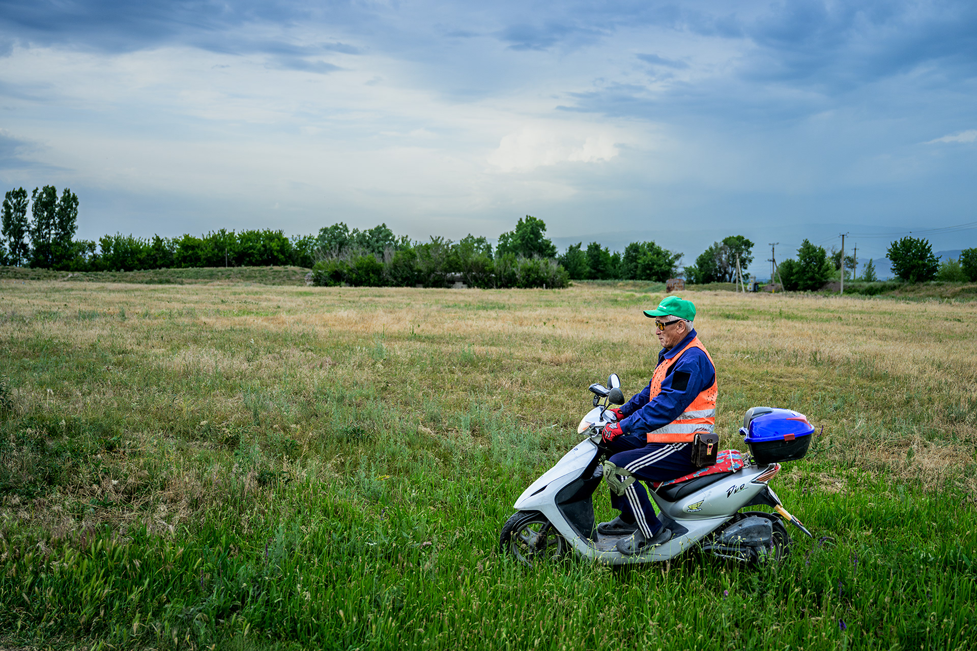 Documentary photography from Kyrgyzstan. An elderly man is riding a scooter across a field.