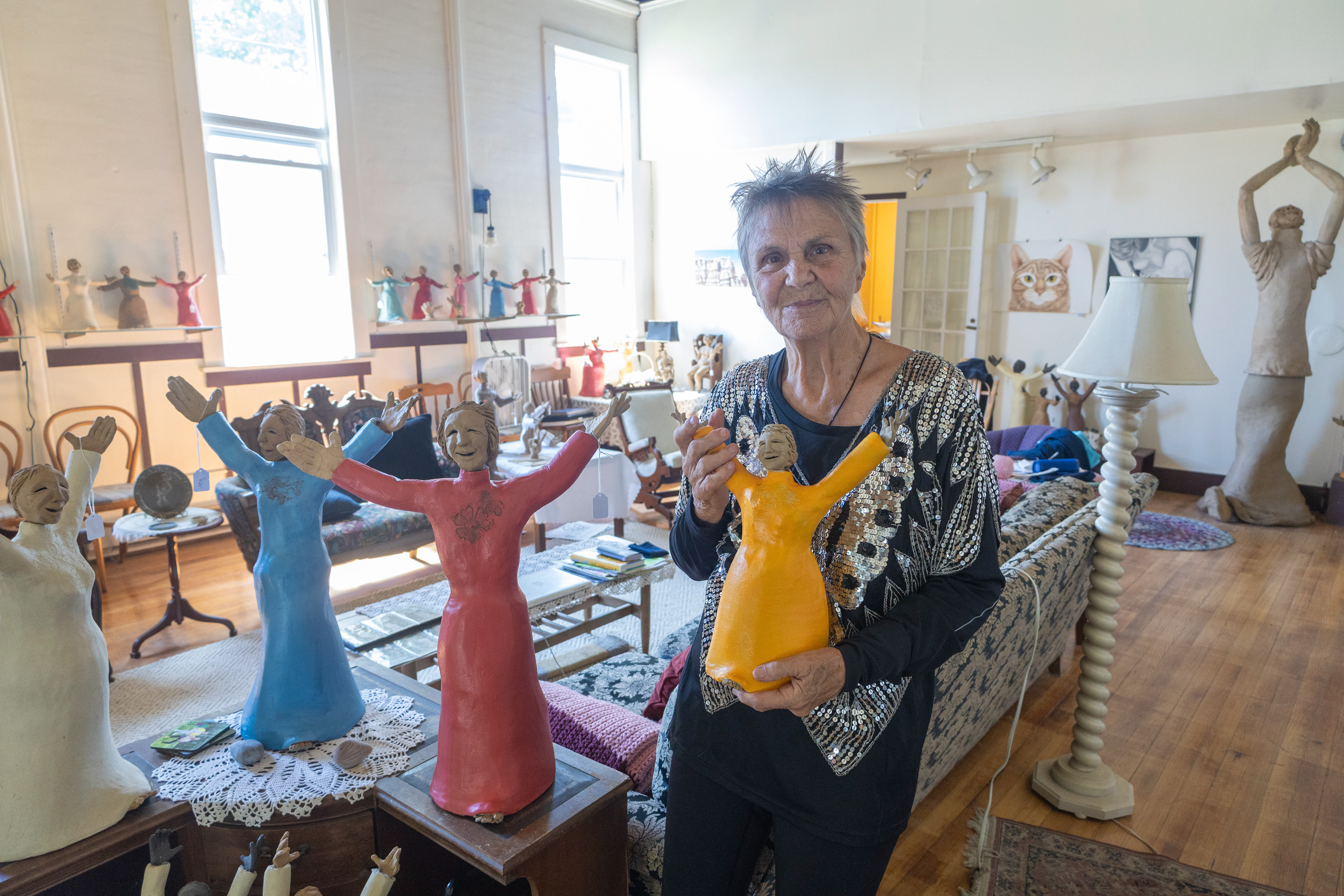 Artist Kirsten Engstrom stands next to her sculptures while holding one.