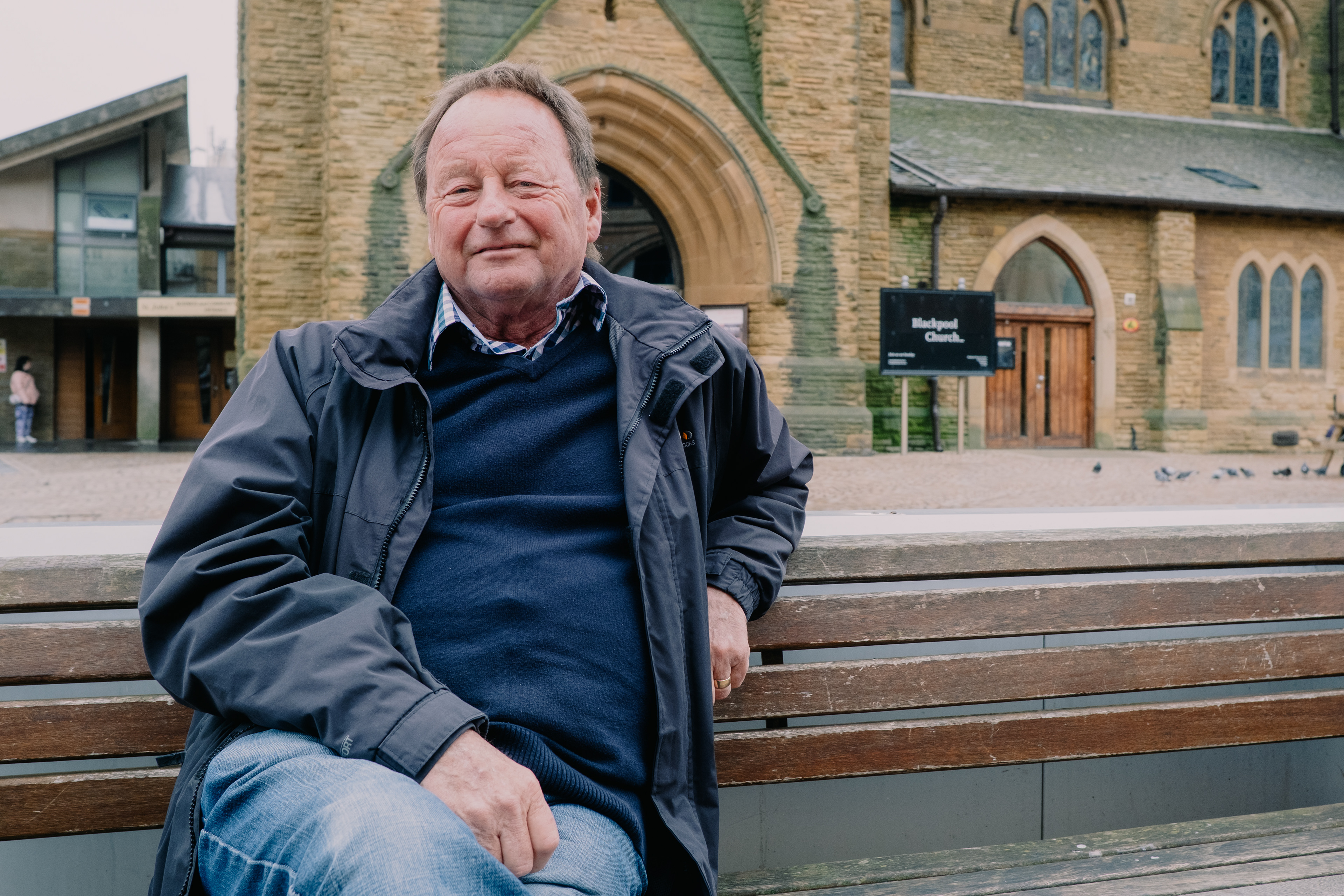 “She loves the shops. I love the benches.” Brian had found his spot. While his wife explored the shops, he settled into his bench and watched the afternoon unfold. The passing crowds gave him company, and he seemed content to let the world move around him.