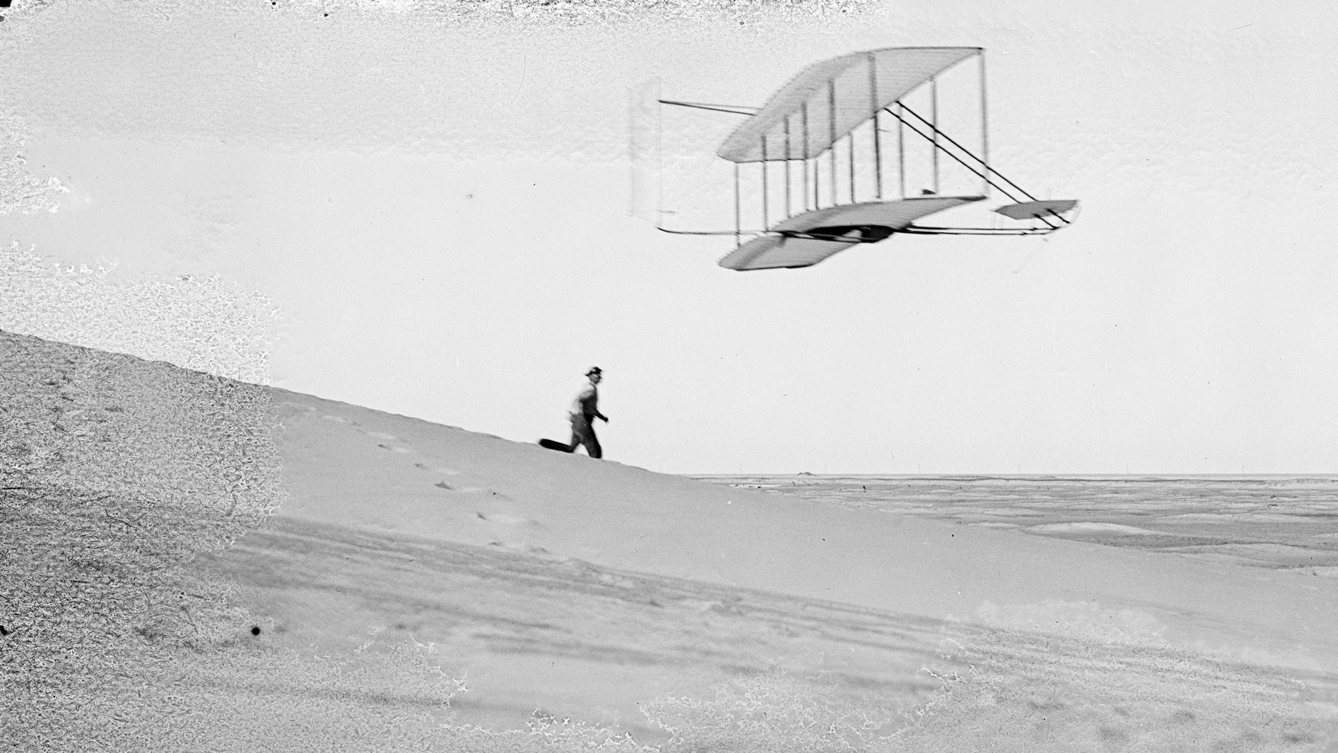 Wilbur flying 1902 glider, Dan Tate running alongside; Big Kill Devil Hill, North Carolina.