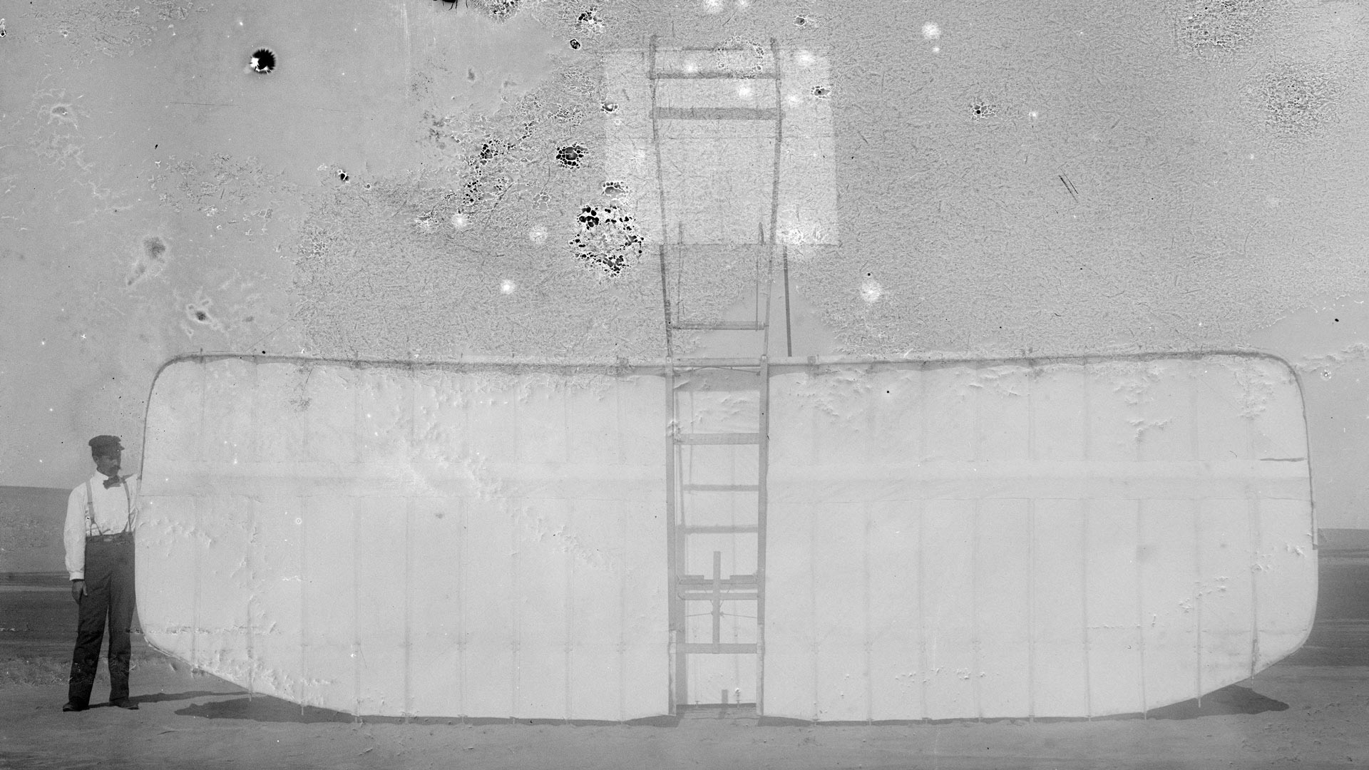 Orville at left wing end of upended glider, bottom view; Kitty Hawk, North Carolina, 1901.