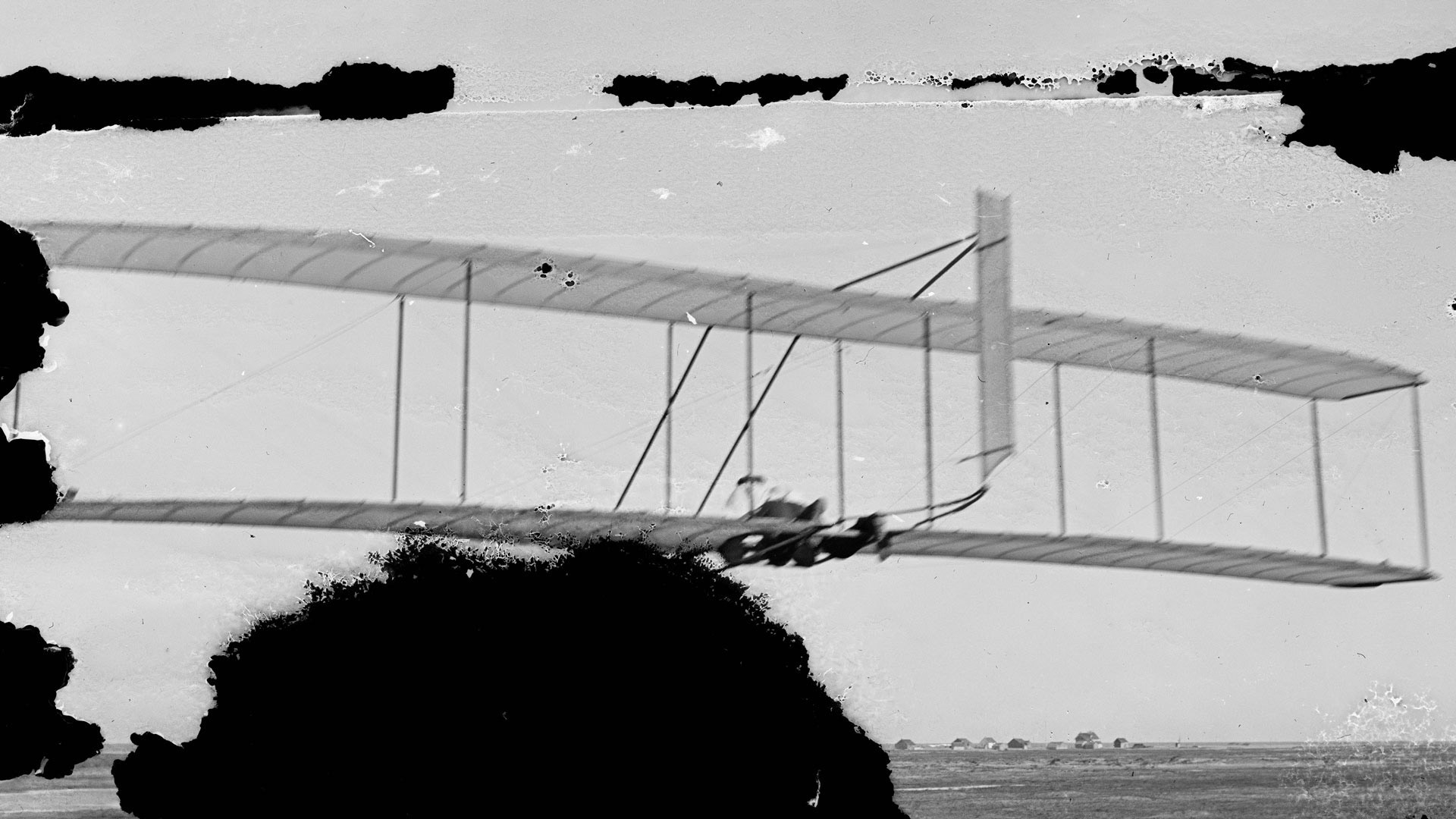 Wilbur Wright gliding, Kitty Hawk Lifesaving Station and Weather Bureau in distance; Kitty Hawk, North Carolina, 1902.