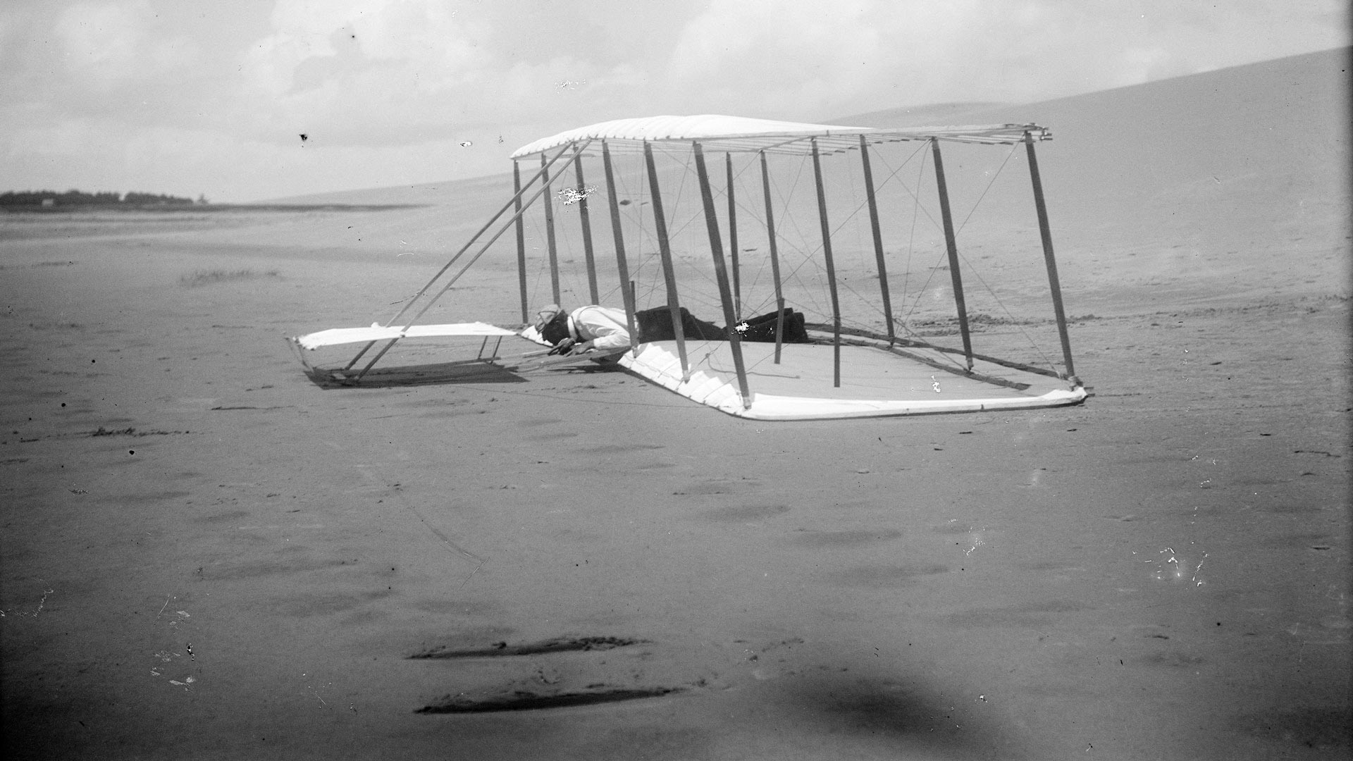 Wilbur Wright on glider just after landing. Skid marks visible behind and in the foreground, Kitty Hawk, North Carolina, 1901.
