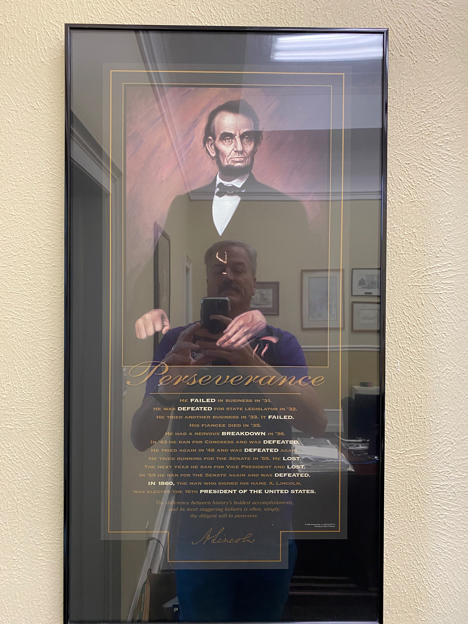 President David Gerlach takes a photo of his framed “Perseverance” poster with his reflection in the image of Abraham Lincoln.