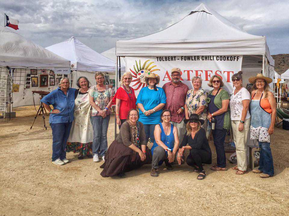Thirteen people lined up in front of a pop up tent displaying their artworks.