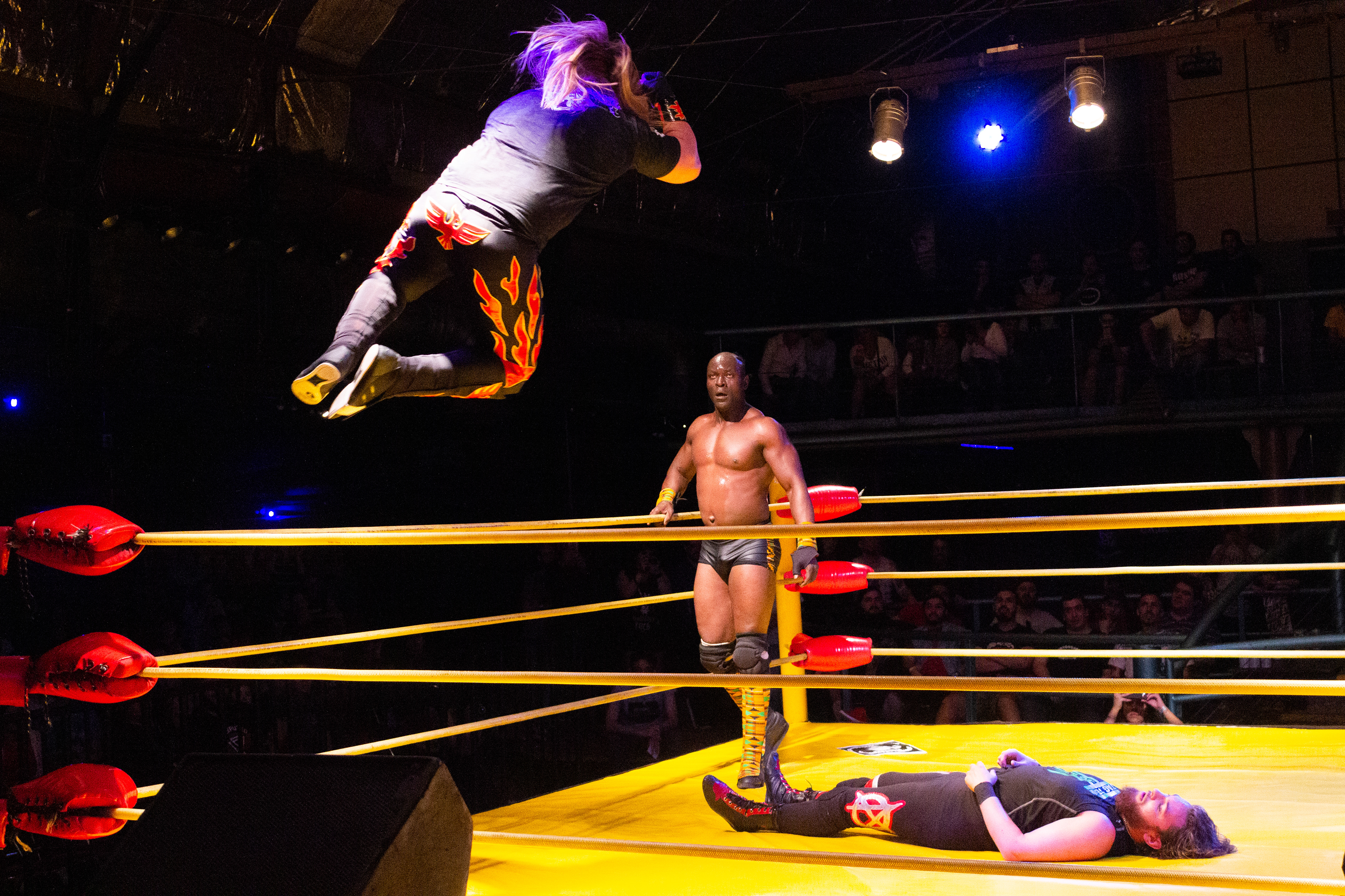Vicente Viloni aplica un codazo volador sobre Rob Dickinson ante la mirada de Musamebe Tutu durante el evento Rock & Wrestling Reloaded 2018 de Lucha Extrema en Ramos Mejía, Buenos Aires, Argentina el 7 de octubre de 2018
